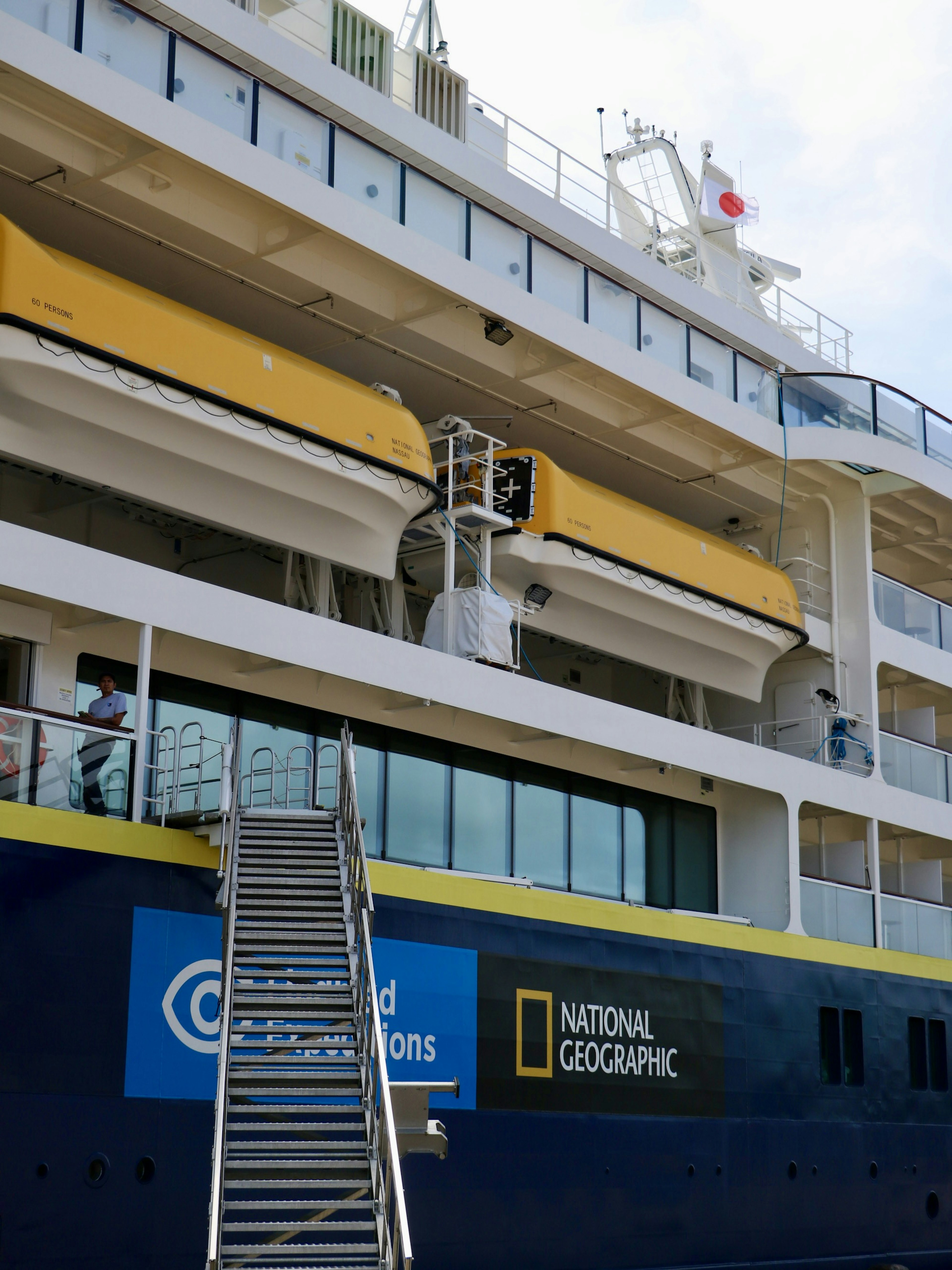 Side view of a National Geographic cruise ship featuring a yellow stripe and a staircase