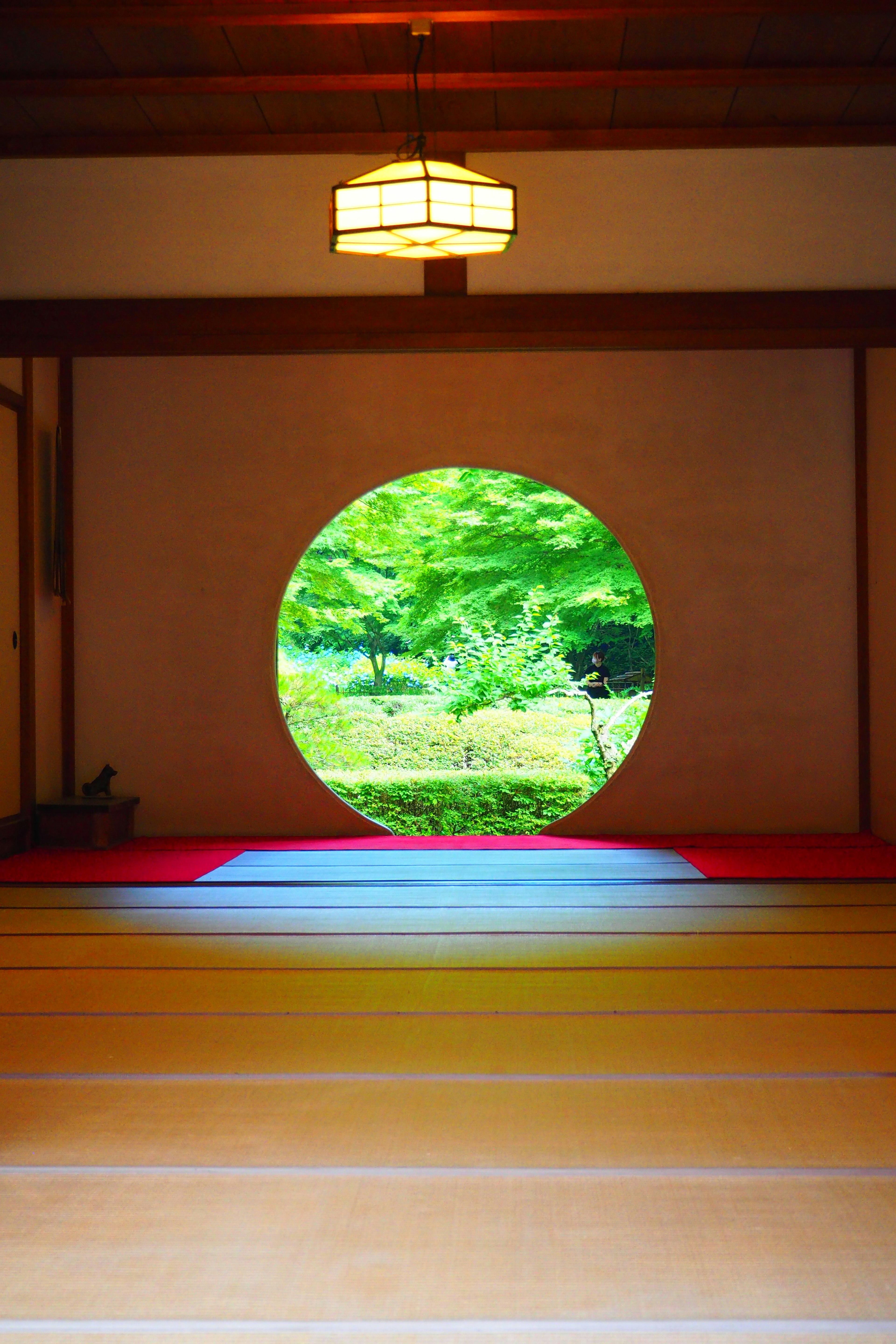 Fenêtre circulaire révélant un jardin verdoyant et une pièce de tatami lumineuse