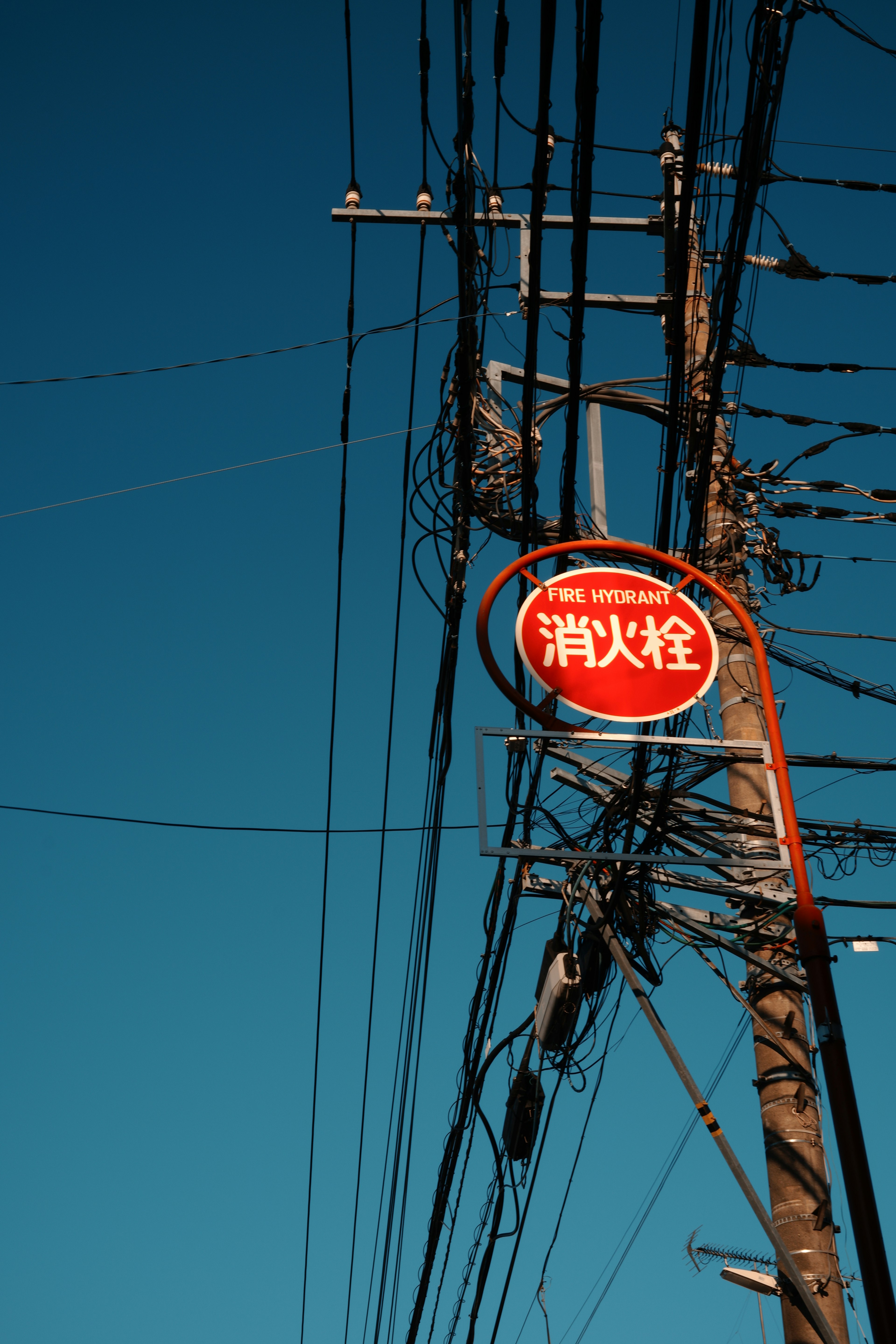 Rotes Schild an einem Strommast mit elektrischen Drähten vor einem blauen Himmel