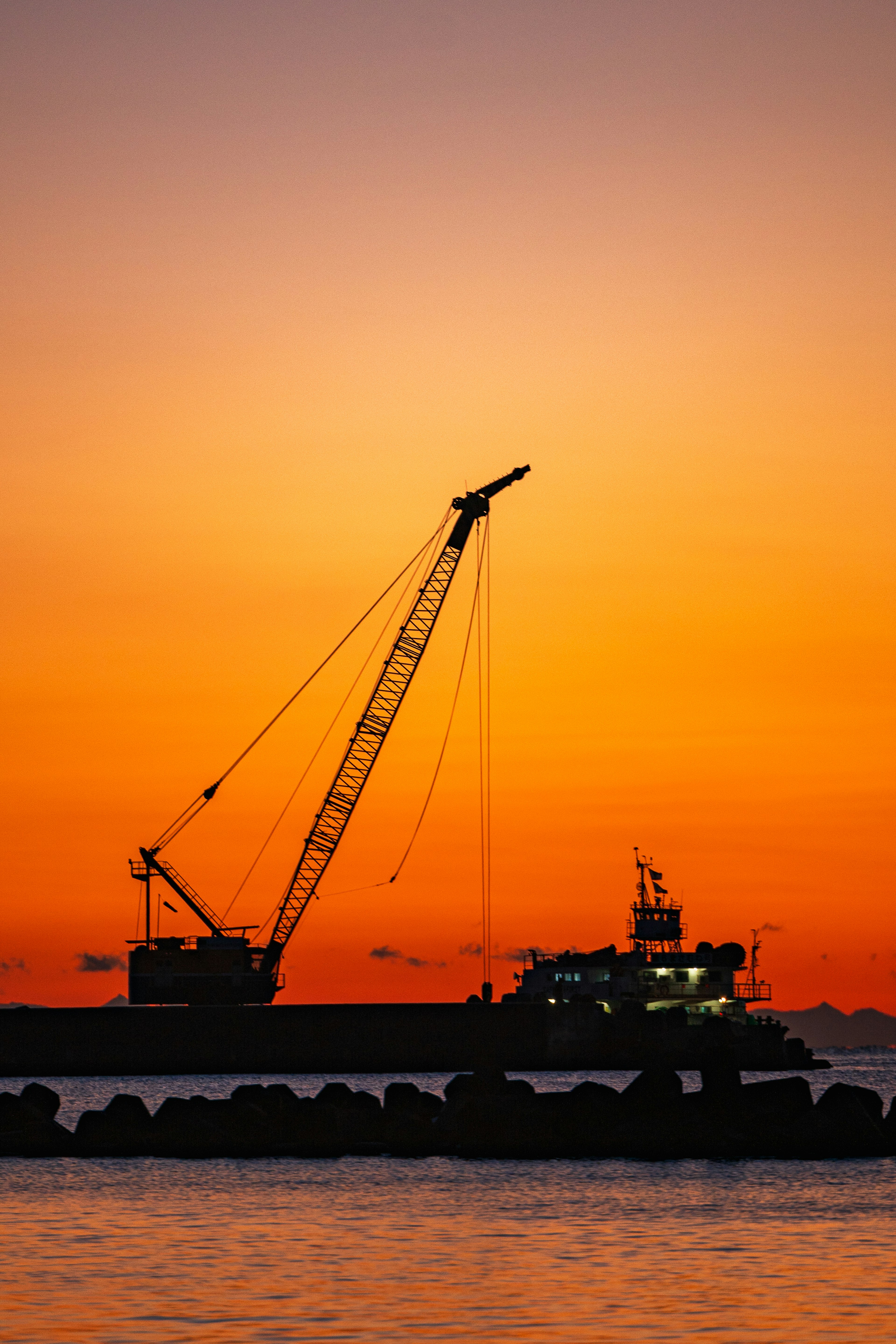 Silhouette di una gru e di una barca contro un tramonto sul mare