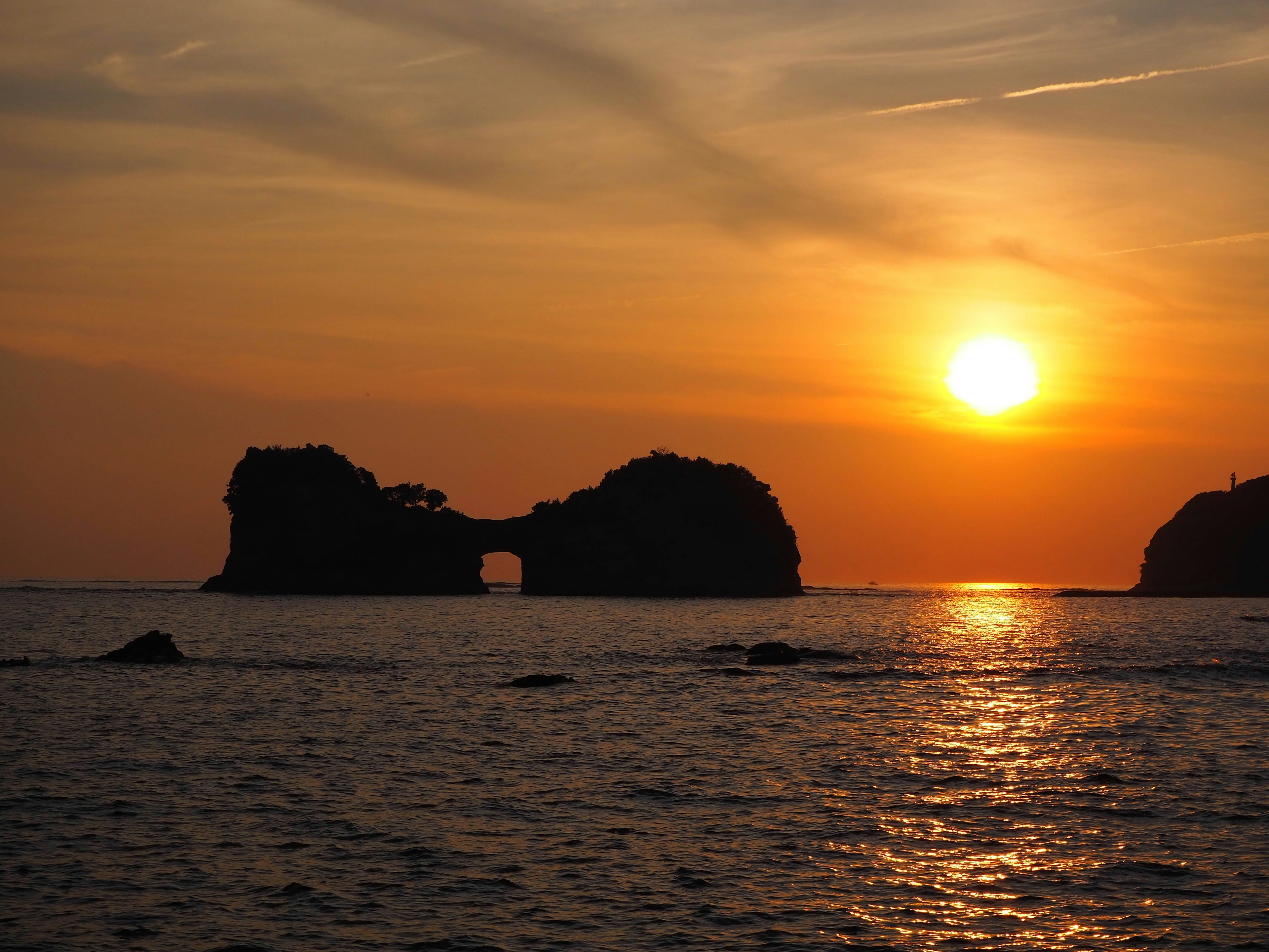 夕日が沈む海に浮かぶ岩のアーチ