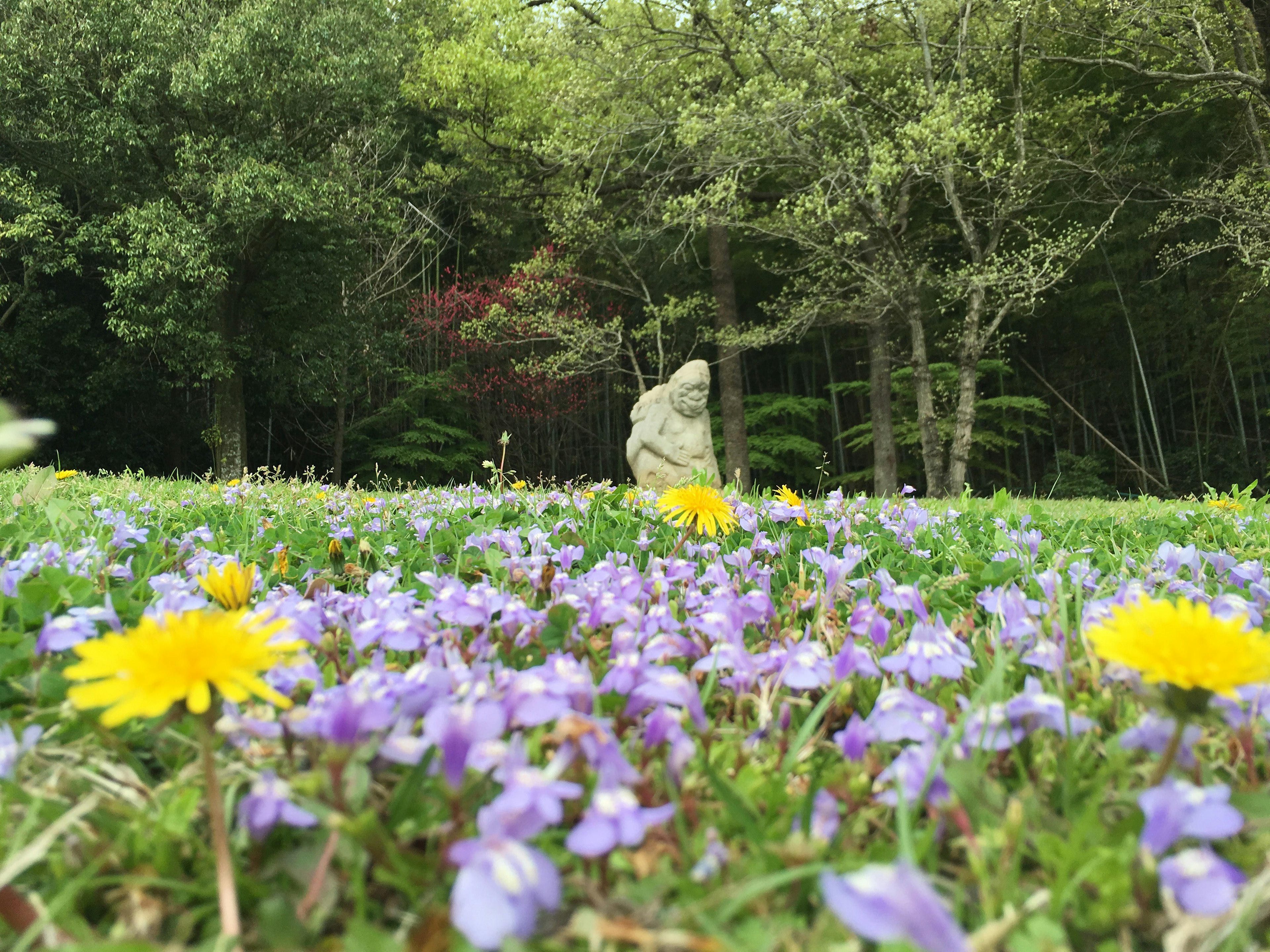 緑の木々の中にある石像と色とりどりの花々の風景