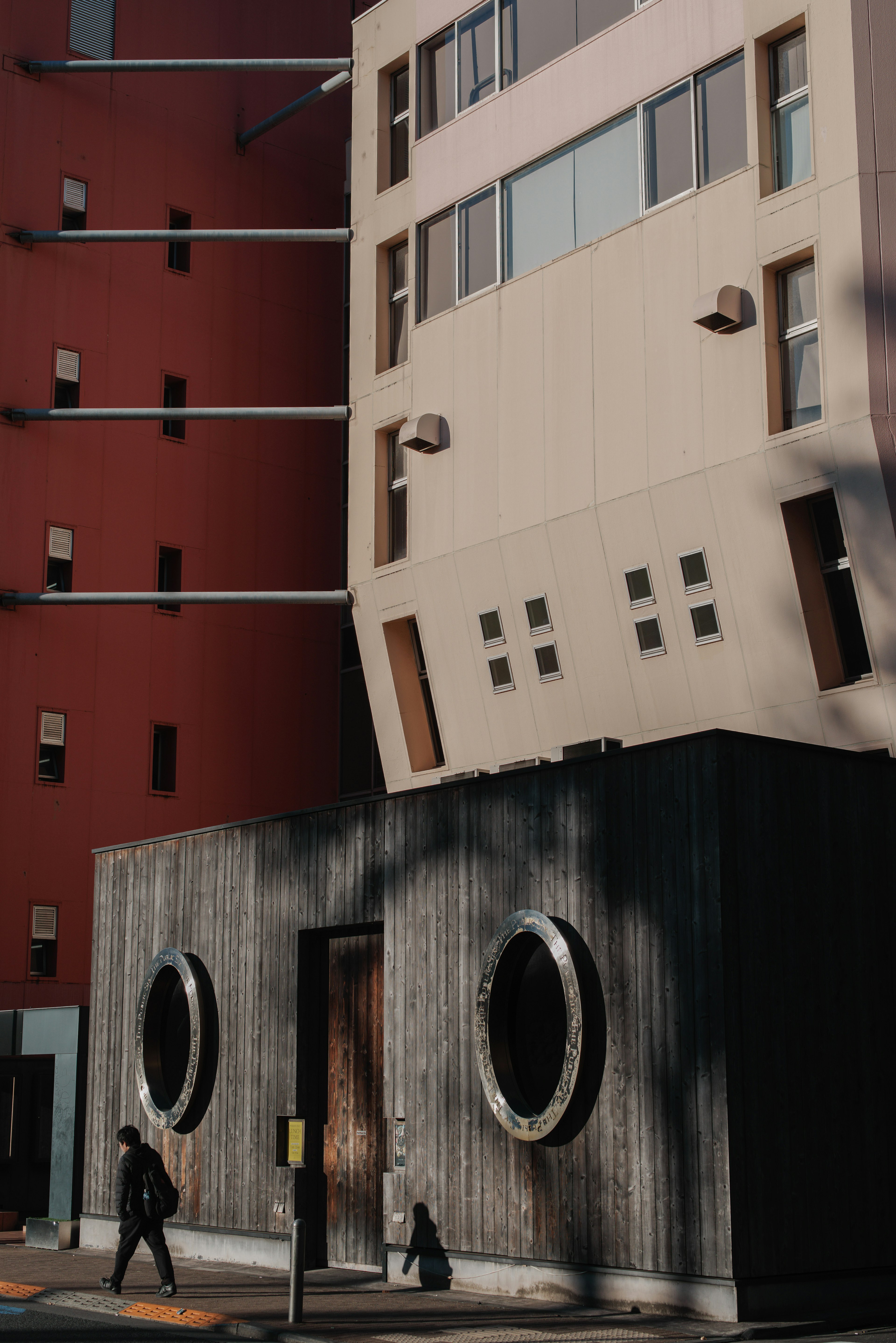 Escena urbana con un edificio moderno inclinado y una pared de concreto con ventanas circulares