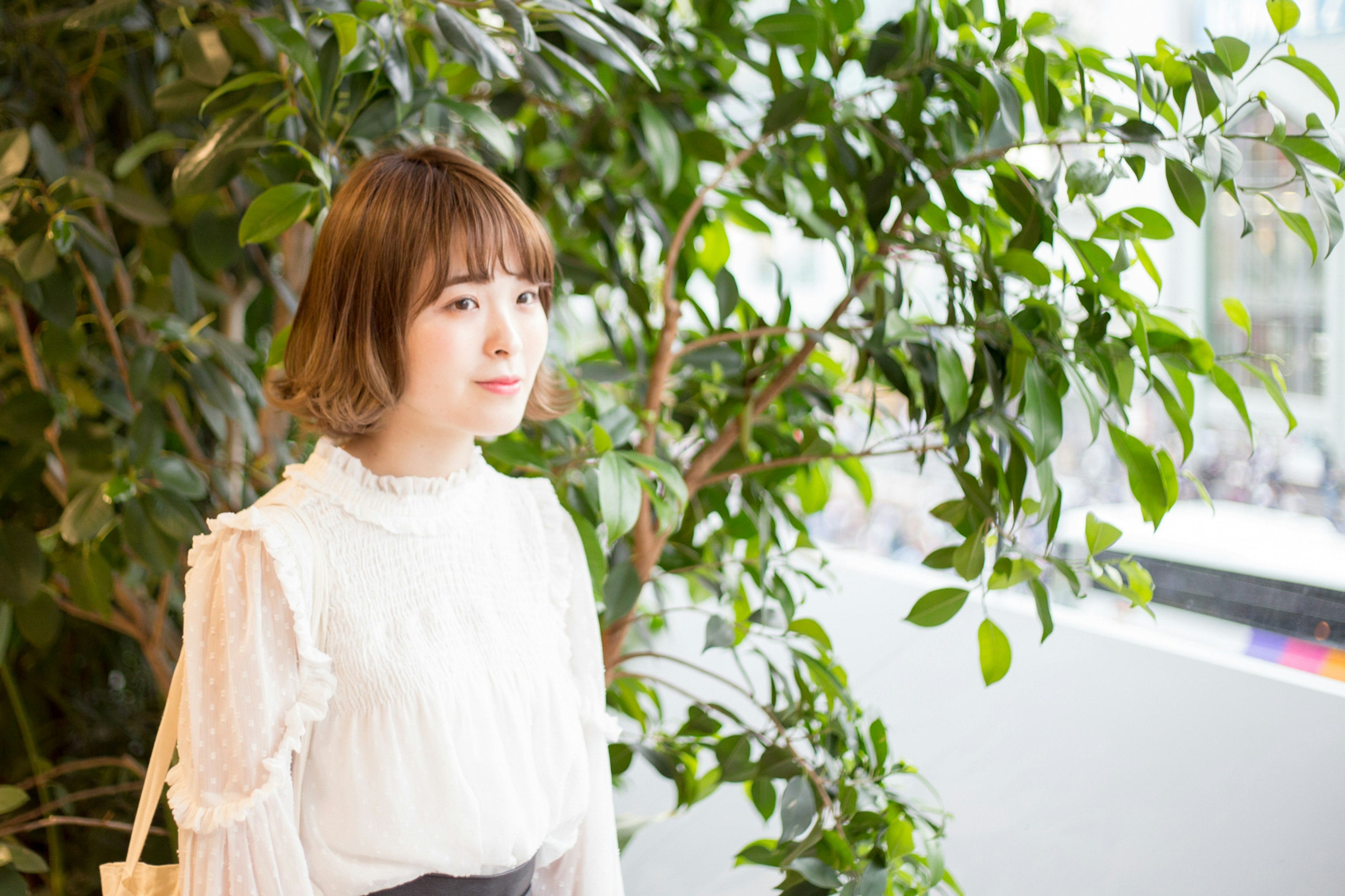 Portrait of a woman standing in front of green plants wearing a white blouse