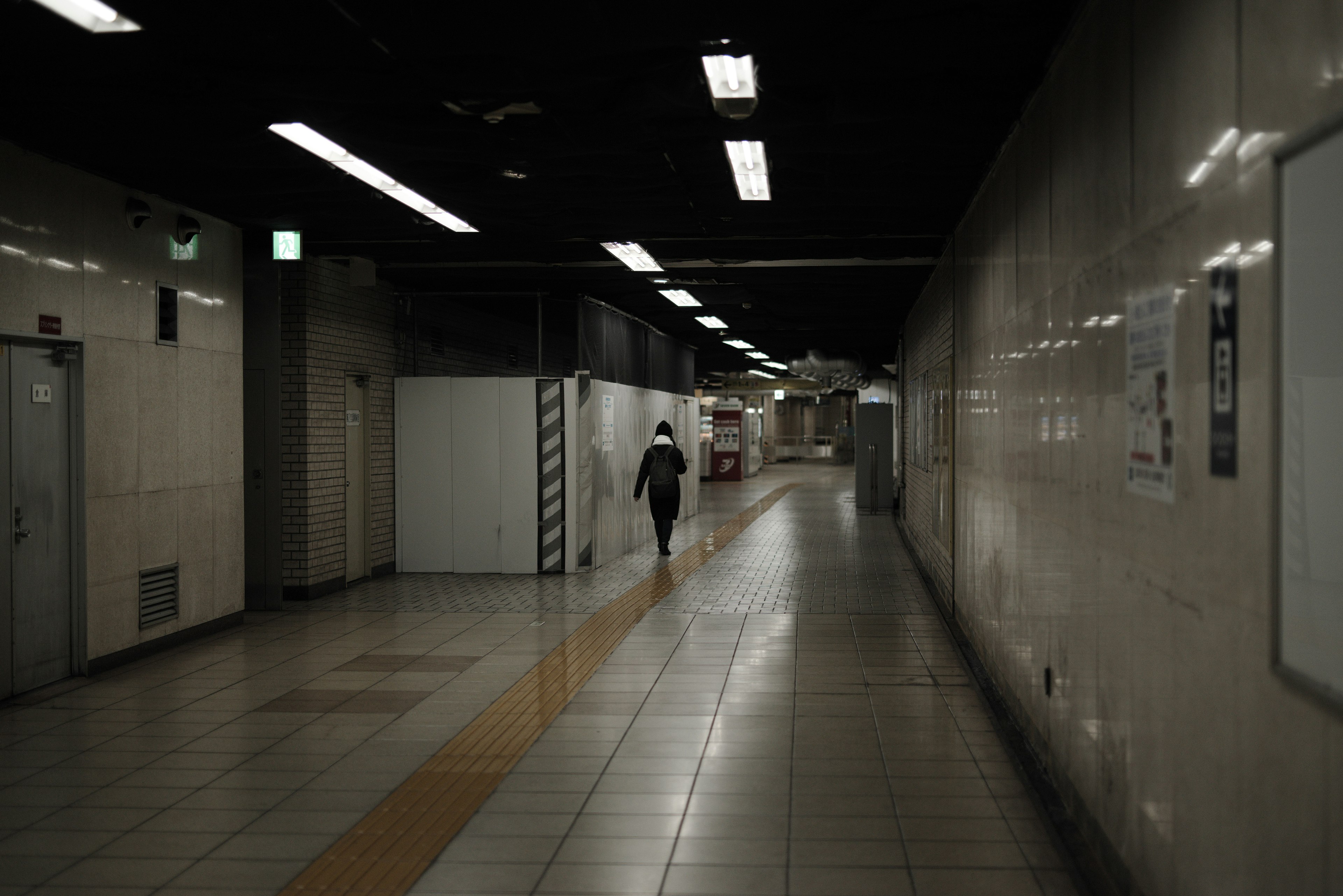 A figure walking in a dimly lit underground corridor with white tiled walls