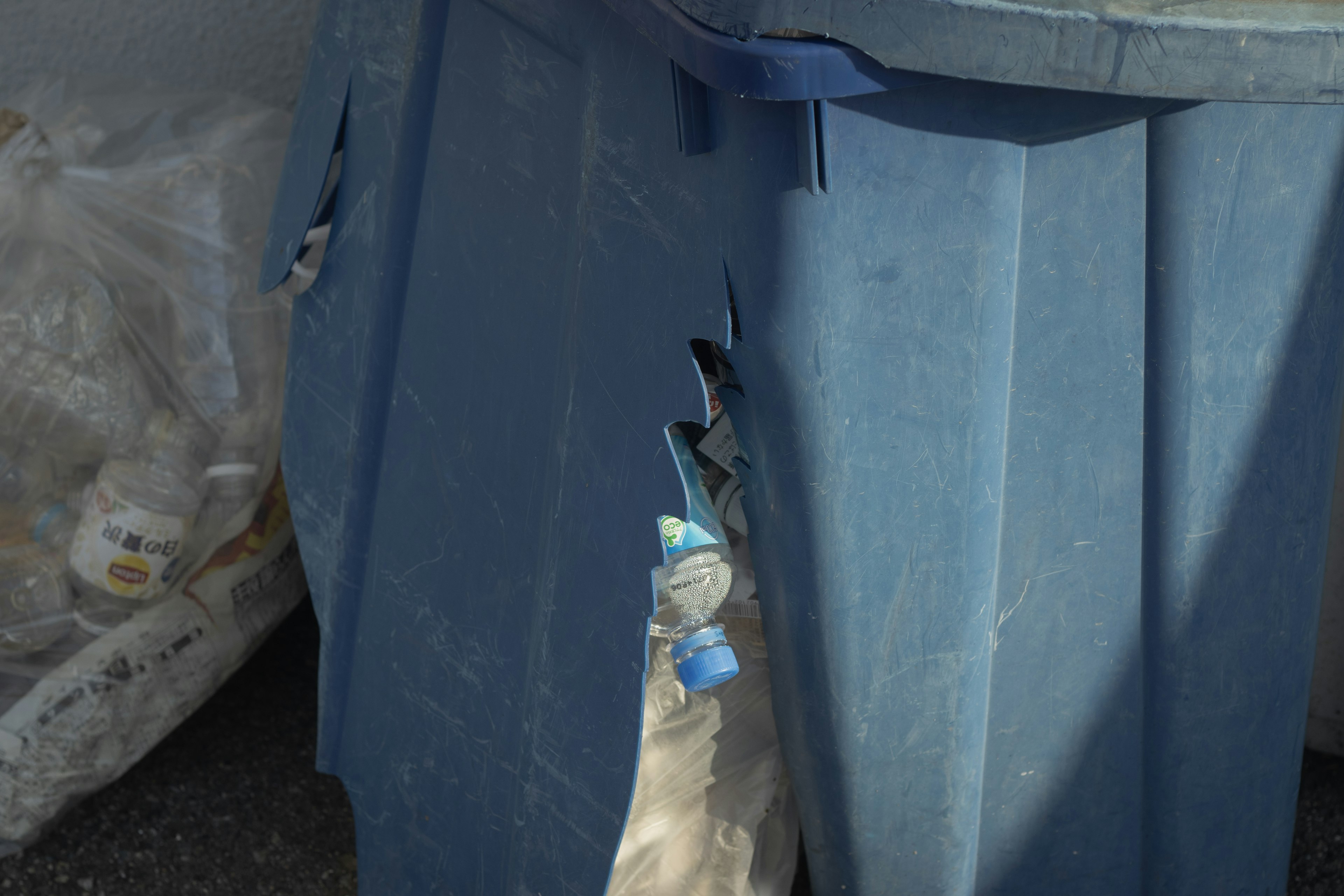 Damaged blue trash bin with visible tears