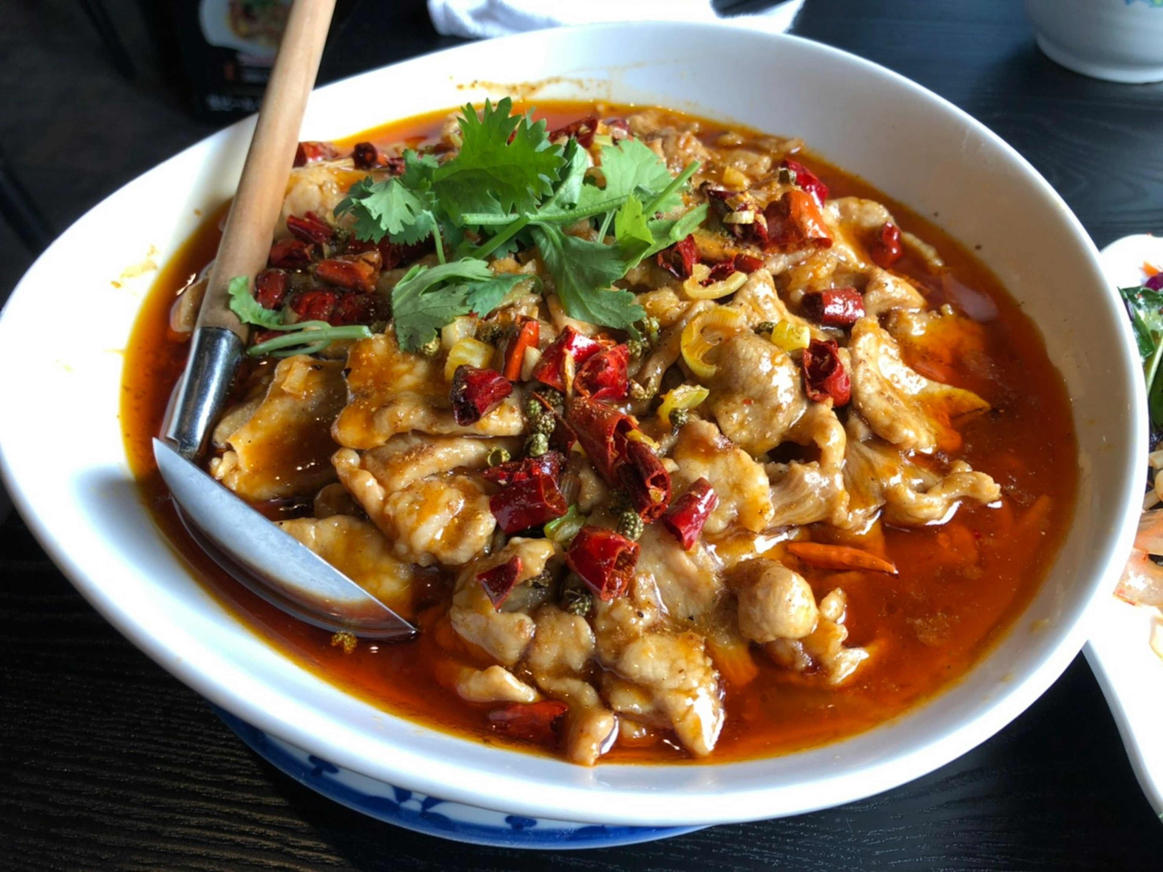 A bowl of spicy chicken dish garnished with cilantro and dried red chilies