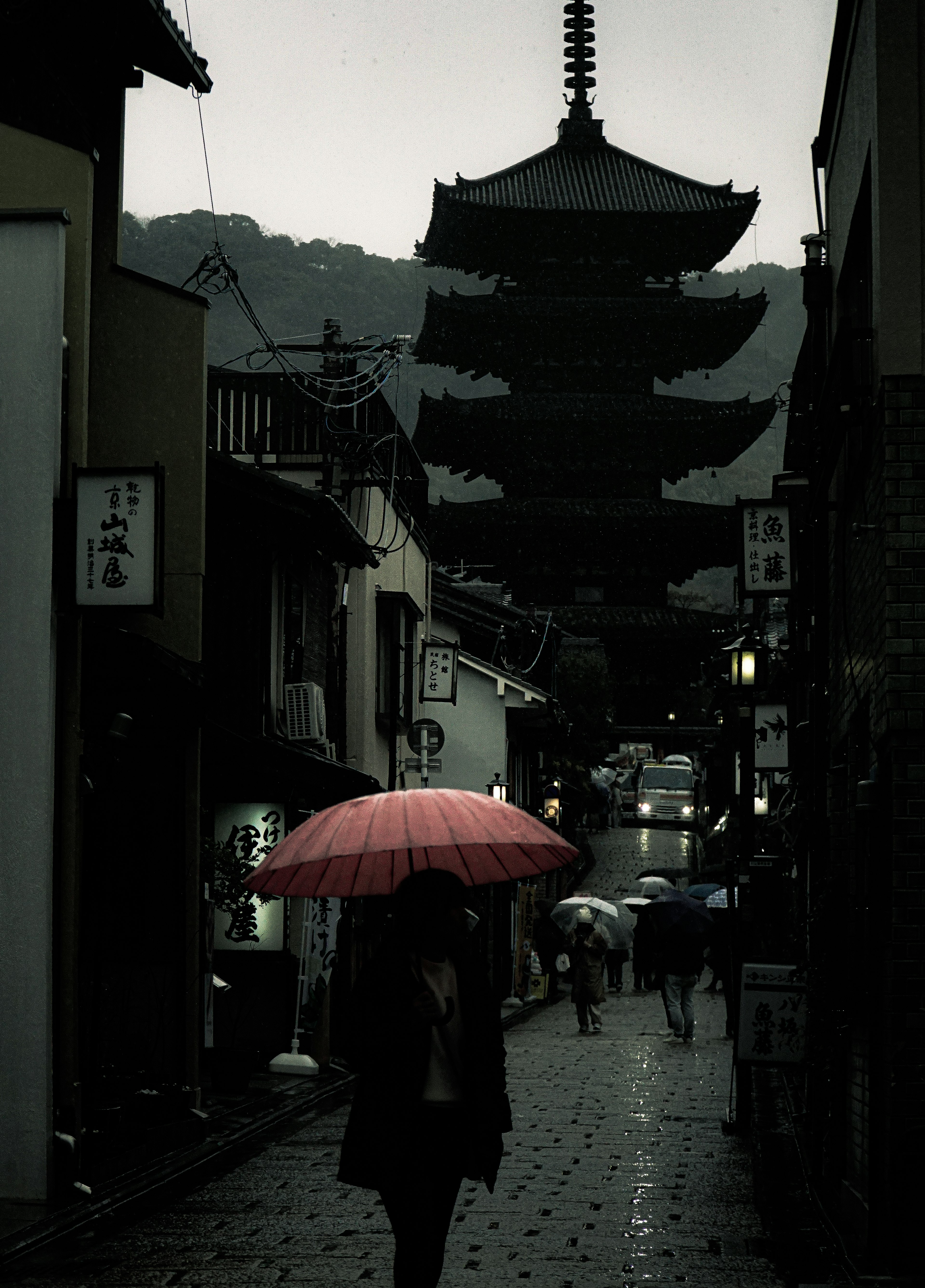 Persona con un paraguas rojo bajo la lluvia y una pagoda de fondo