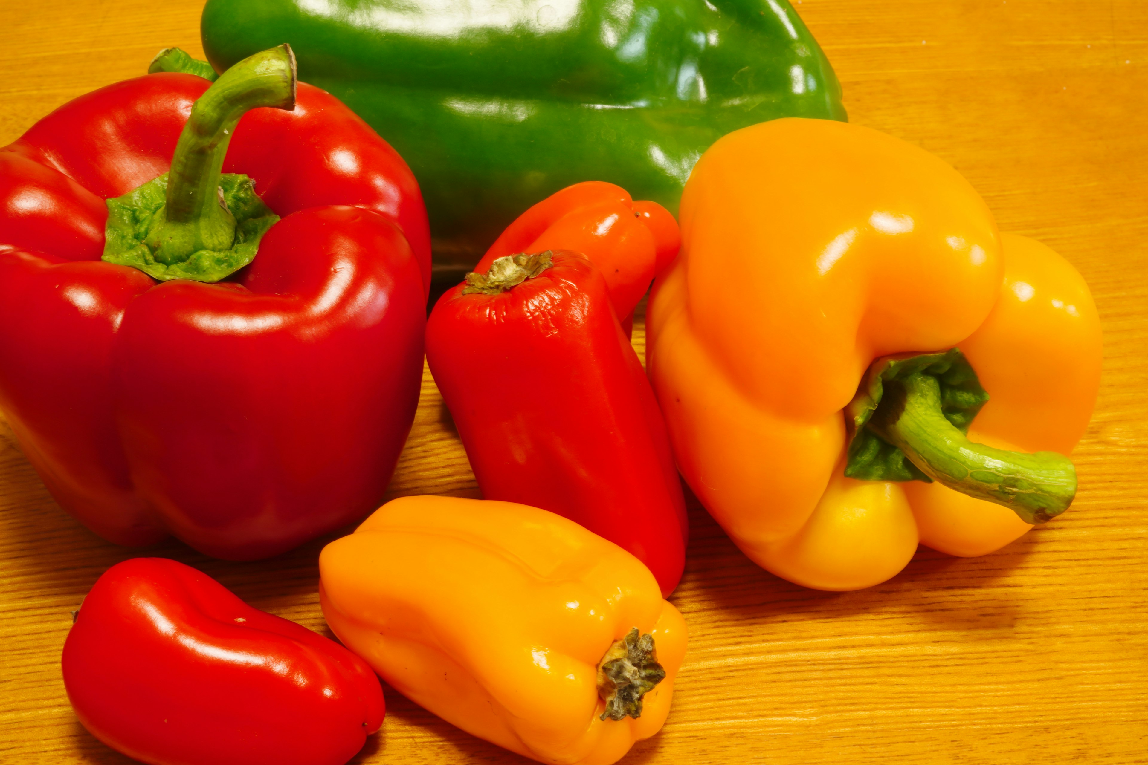 Red, yellow, and green bell peppers along with small peppers arranged on a wooden surface