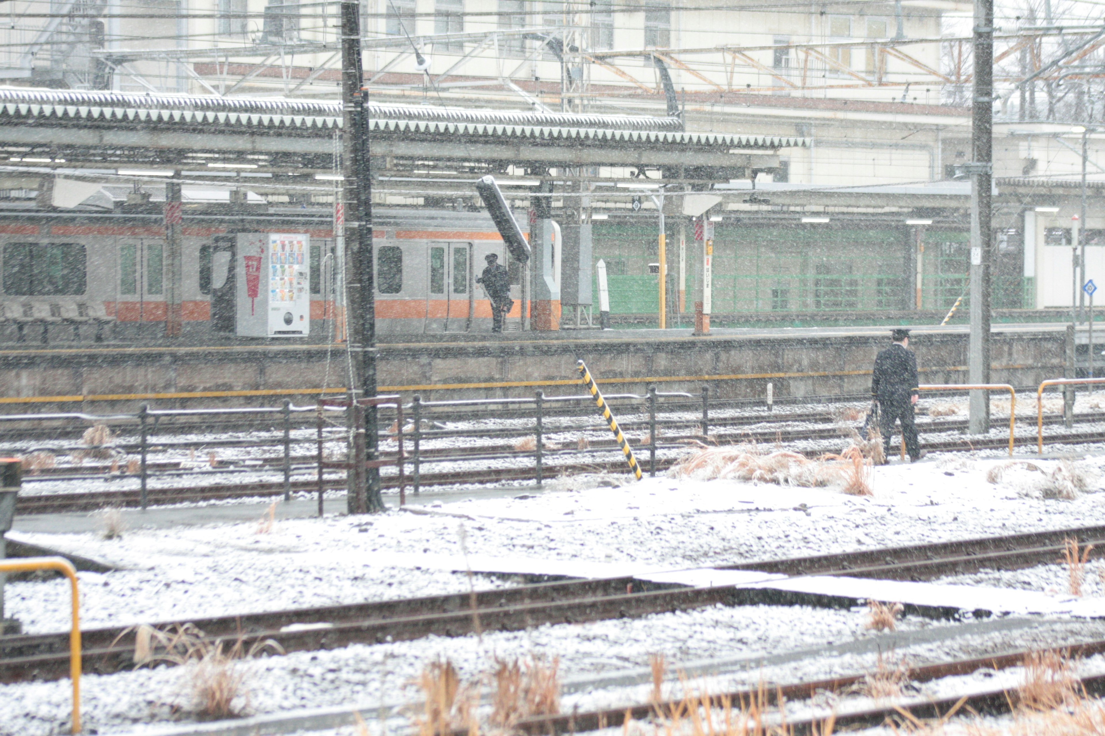 雪が降る駅のプラットフォームに立つ人々と列車