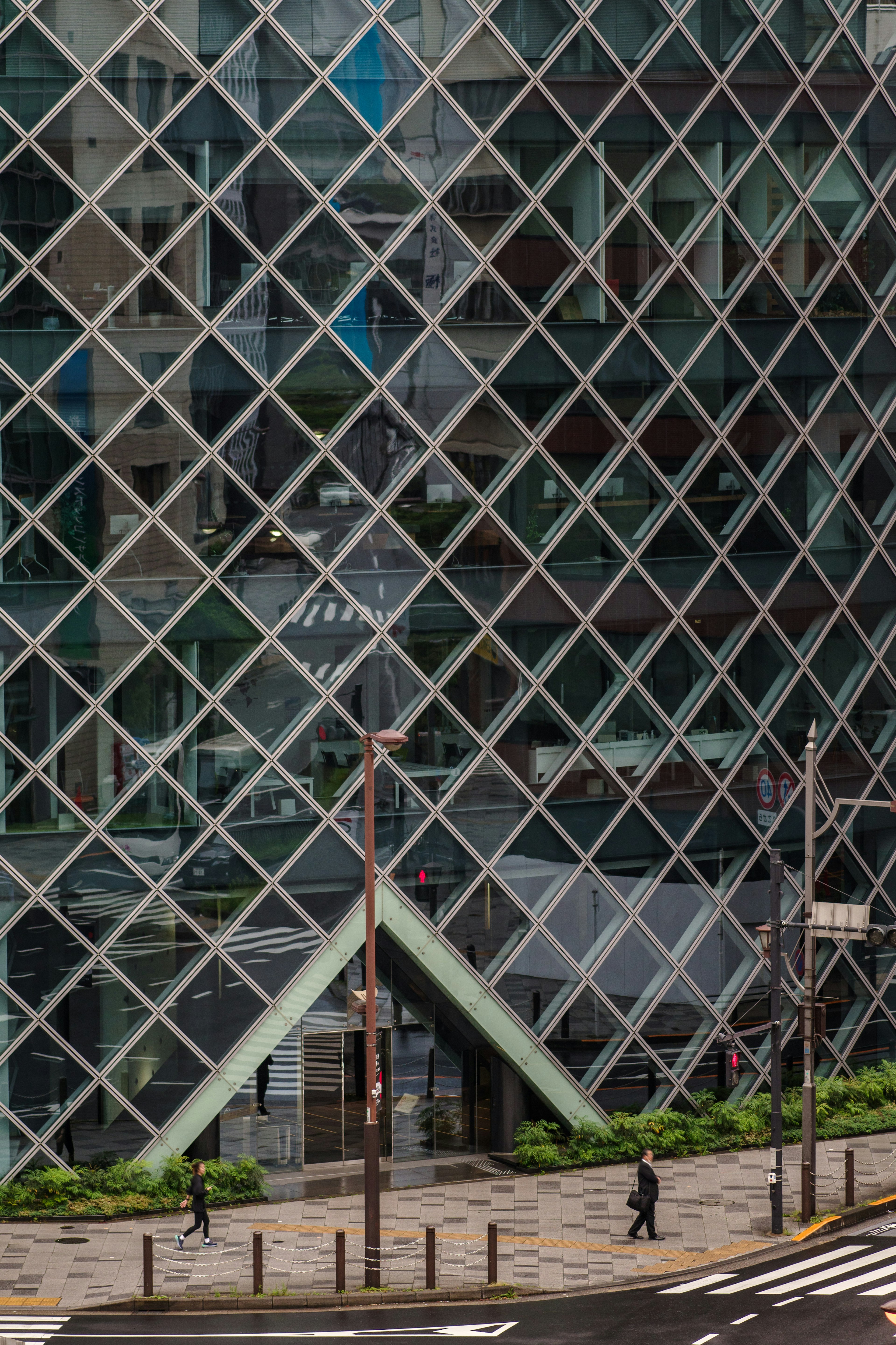 Parte de un edificio moderno con fachada de vidrio y un techo verde diagonal con reflejos