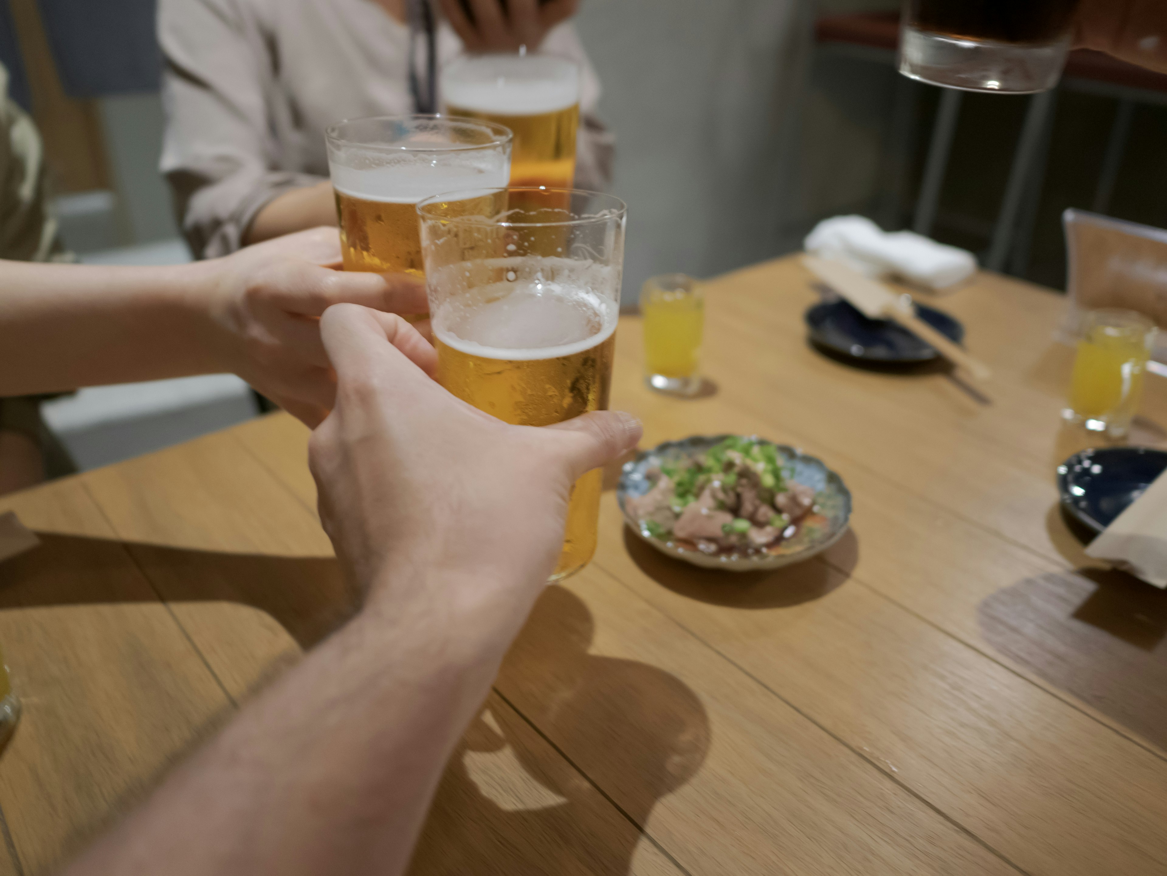 ビールを乾杯する手と料理があるテーブルのシーン