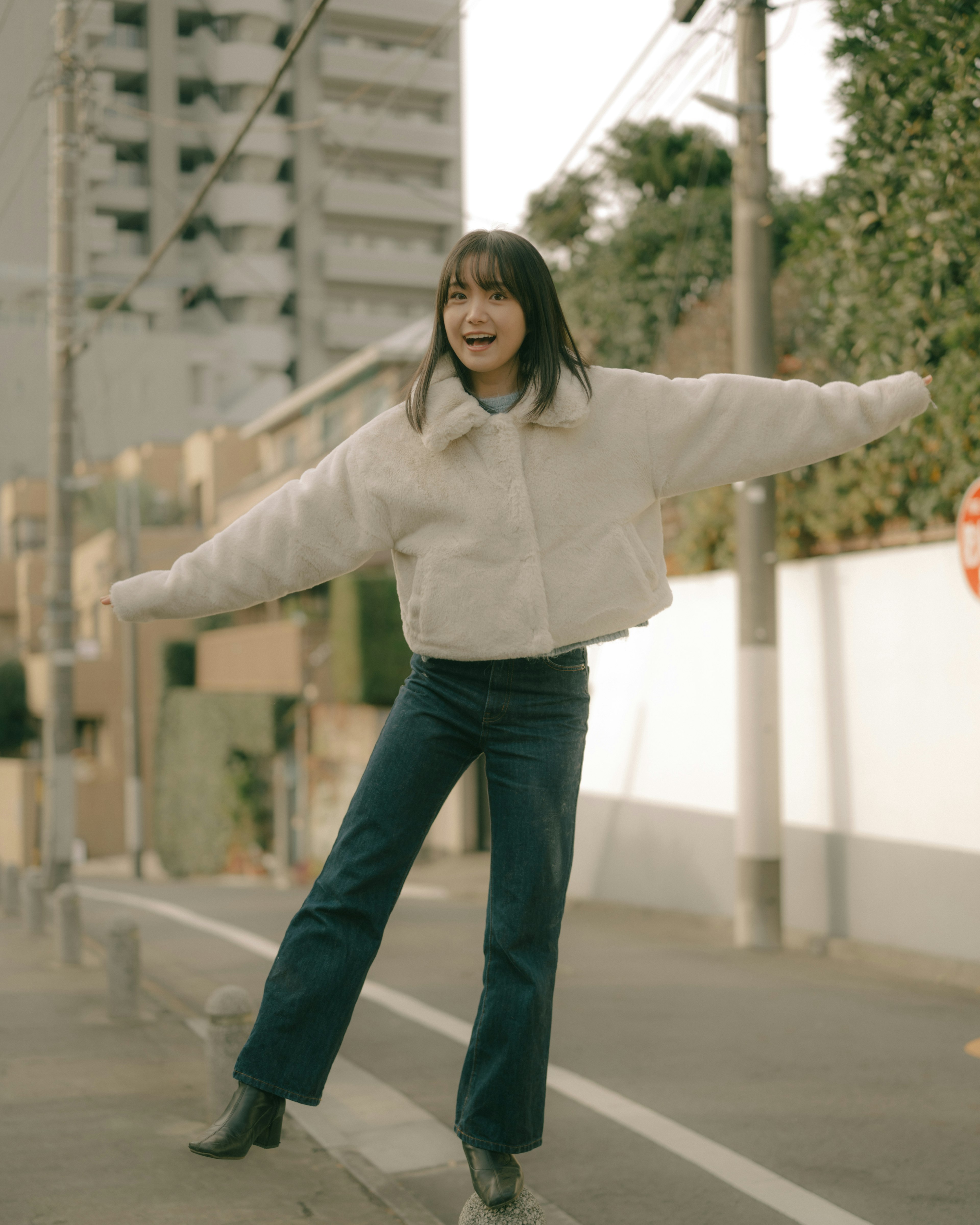 A woman joyfully posing in the street wearing a soft white jacket and denim jeans