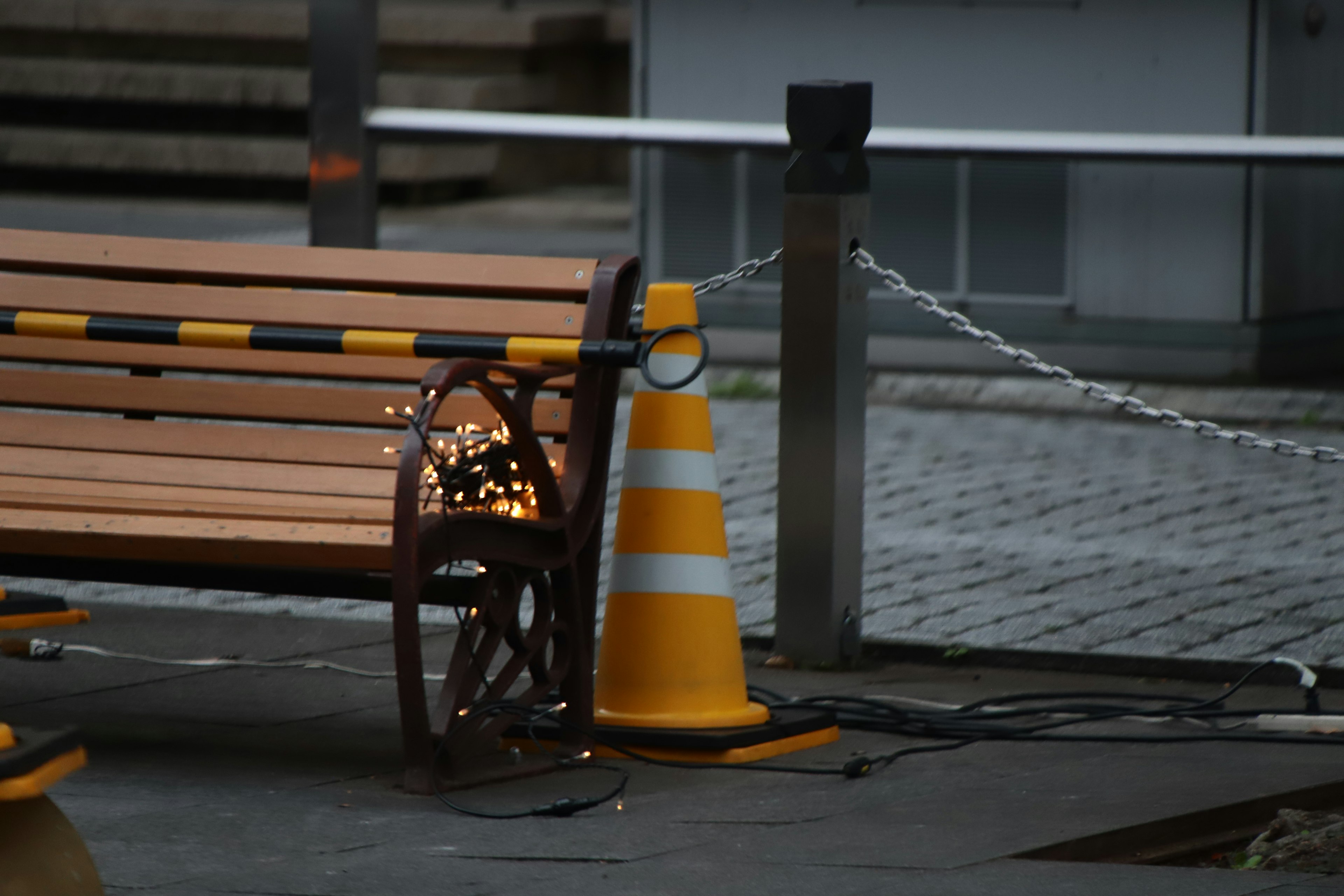 A park bench next to an orange traffic cone with lights