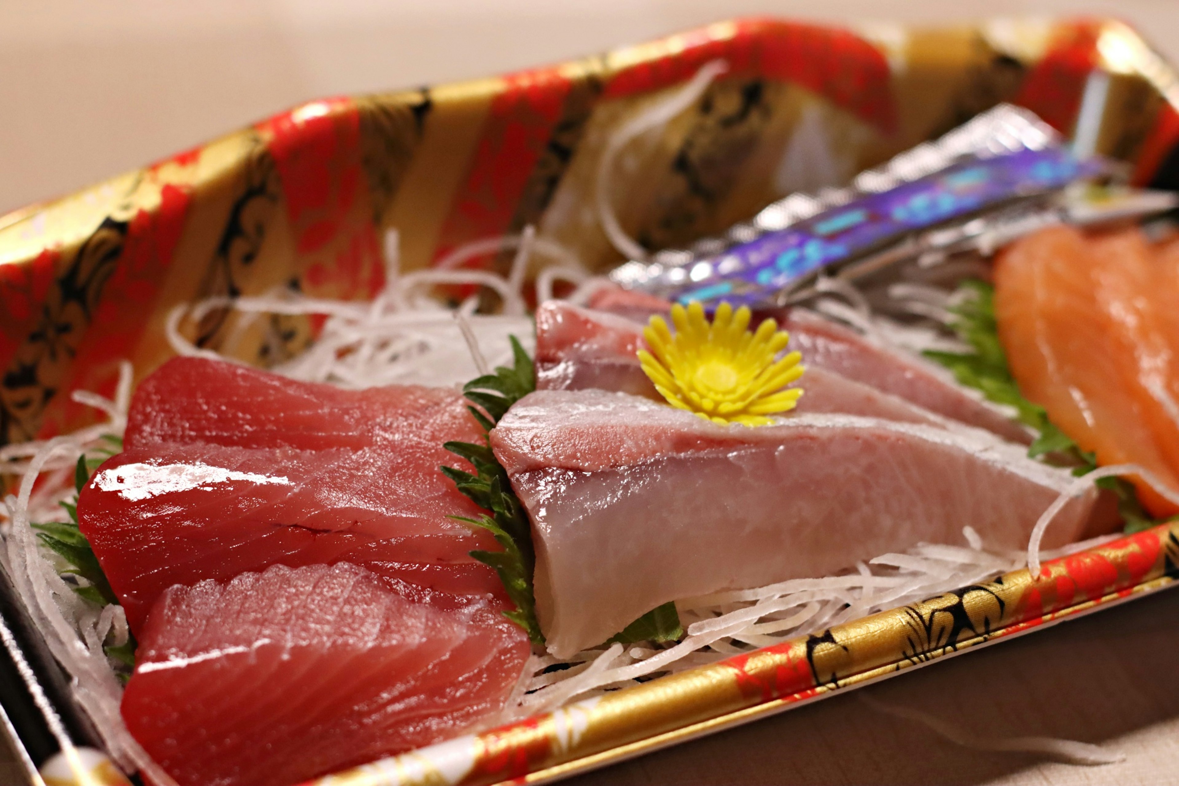 Piring sashimi segar dengan irisan tuna dan hiasan bunga kuning