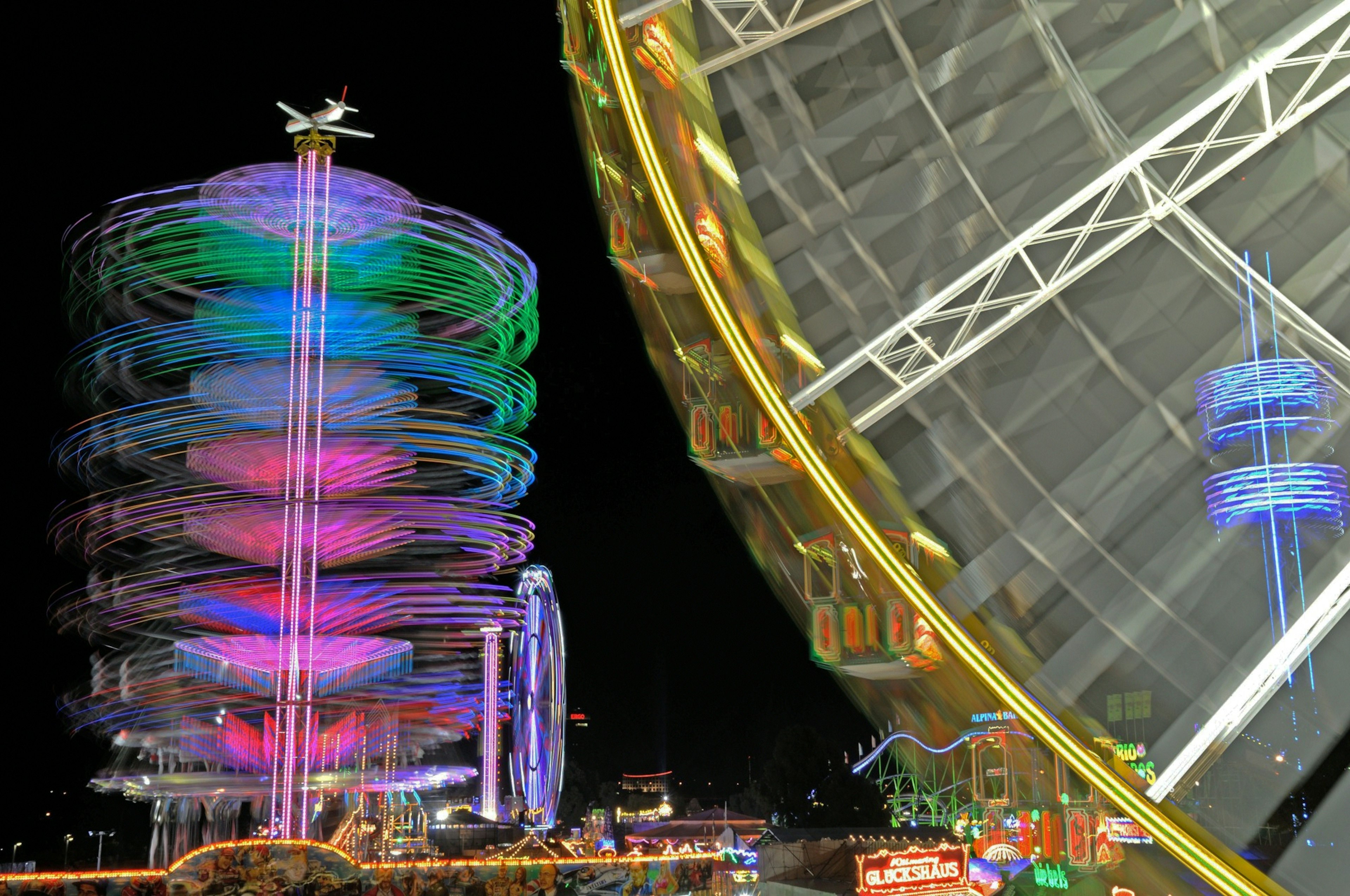 Colorful amusement park rides at night featuring a large Ferris wheel and spinning attraction