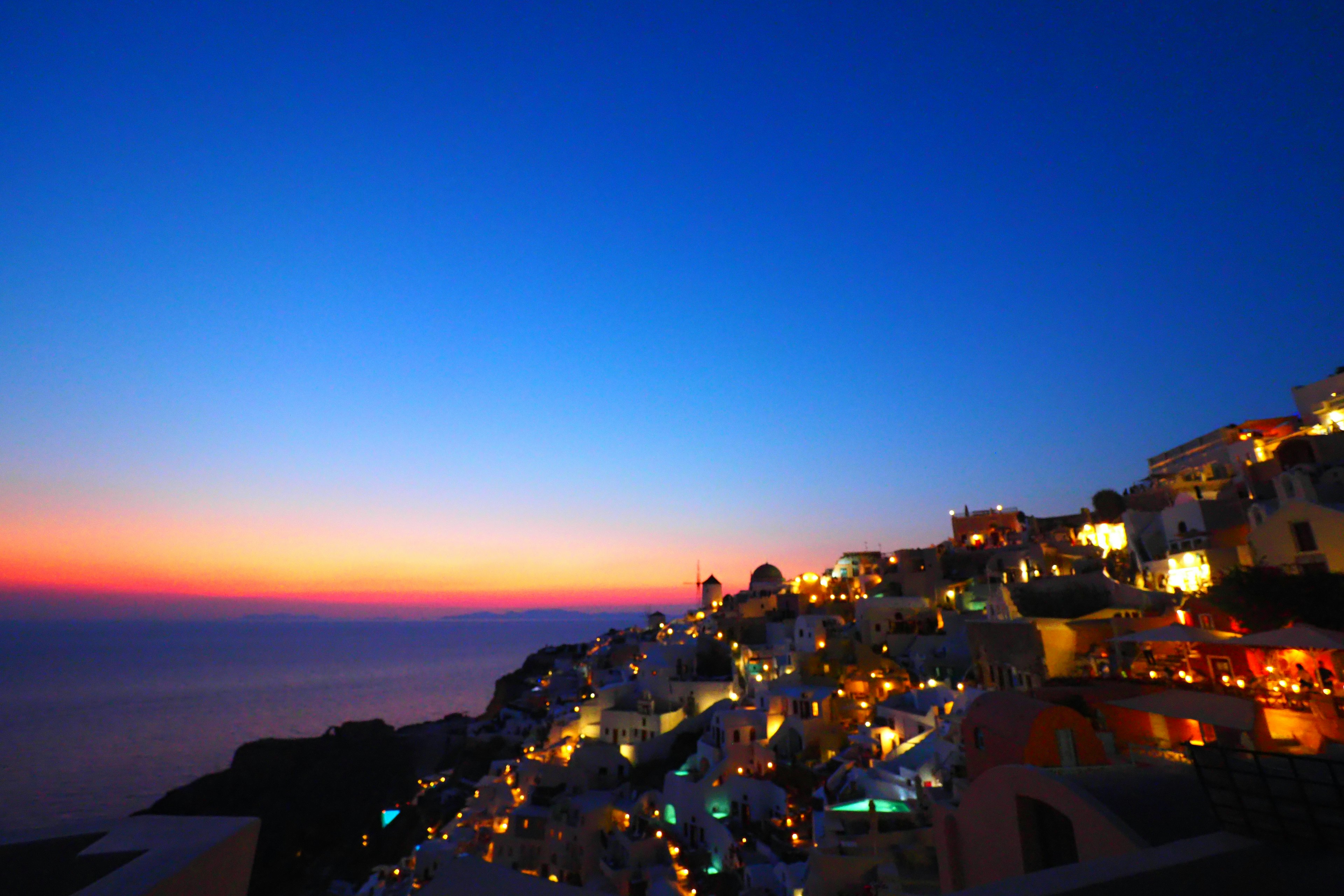 Belle vue du coucher de soleil sur l'île de Santorin avec des lampadaires lumineux et une mer bleu profond