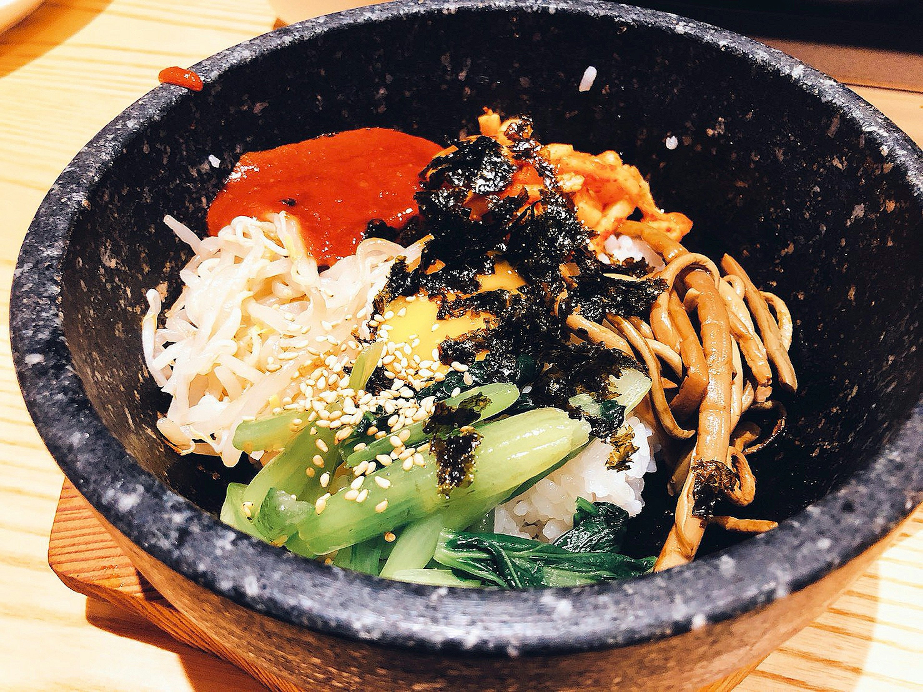 Stone bowl filled with bibimbap topped with vegetables and sauces