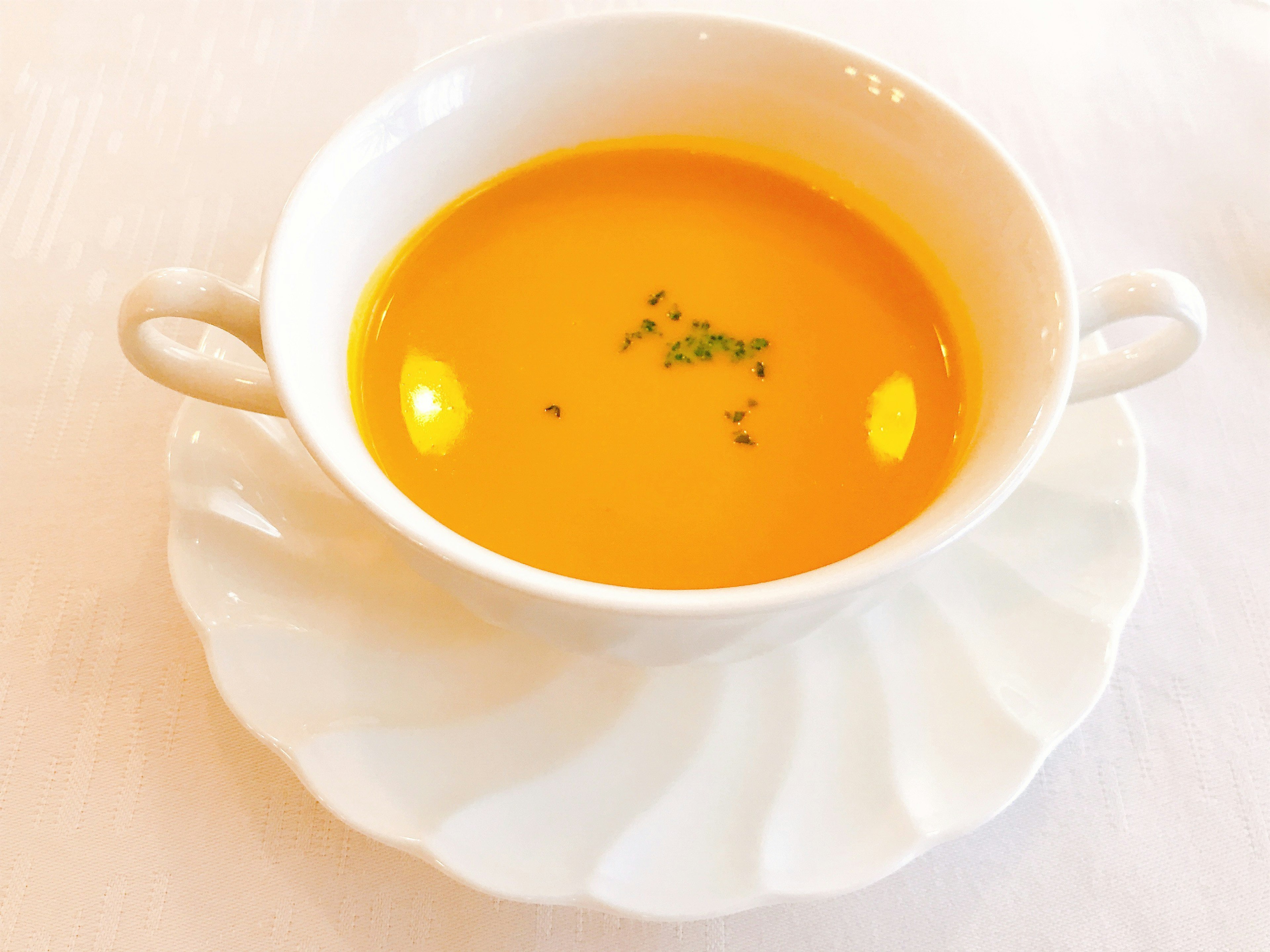 Orange soup served in a white bowl on a decorative plate