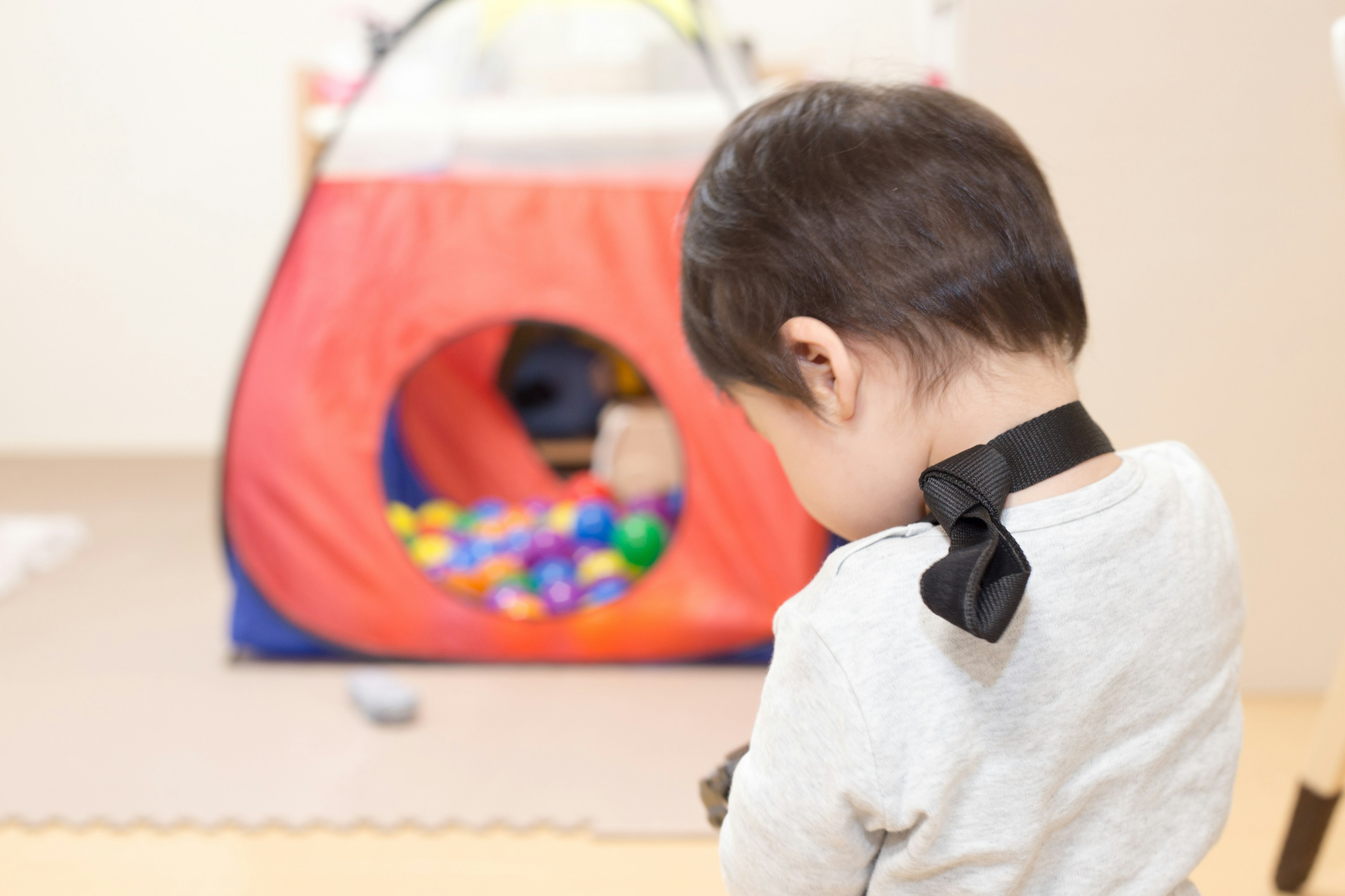 Bambino con un papillon nero di spalle e palline colorate in una tenda