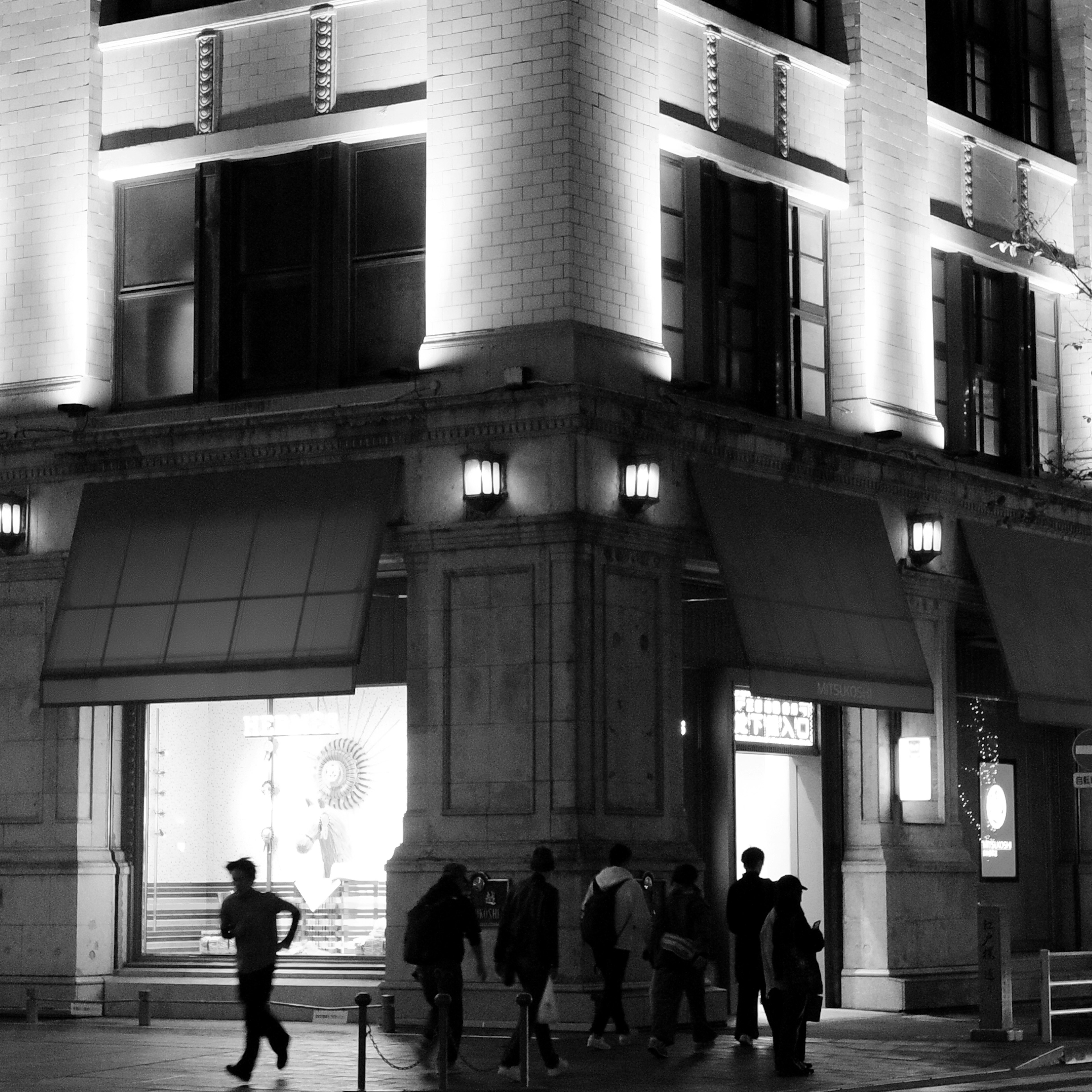 Foto en blanco y negro de una esquina de la calle con un edificio iluminado y peatones