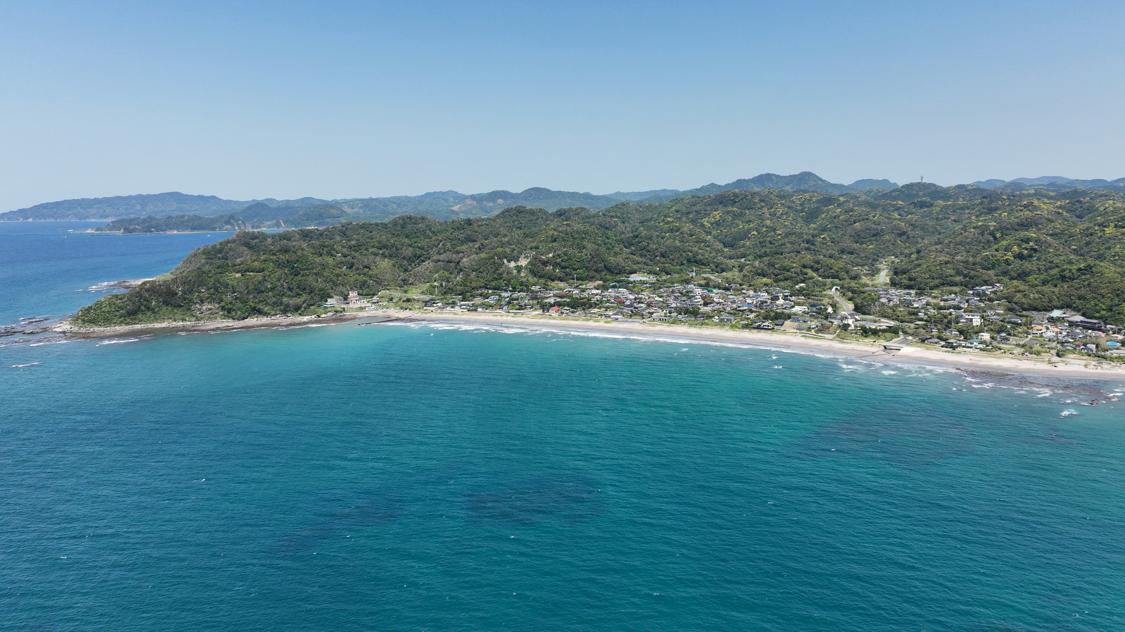 Vue aérienne d'une plage entourée de mer bleue et de collines vertes