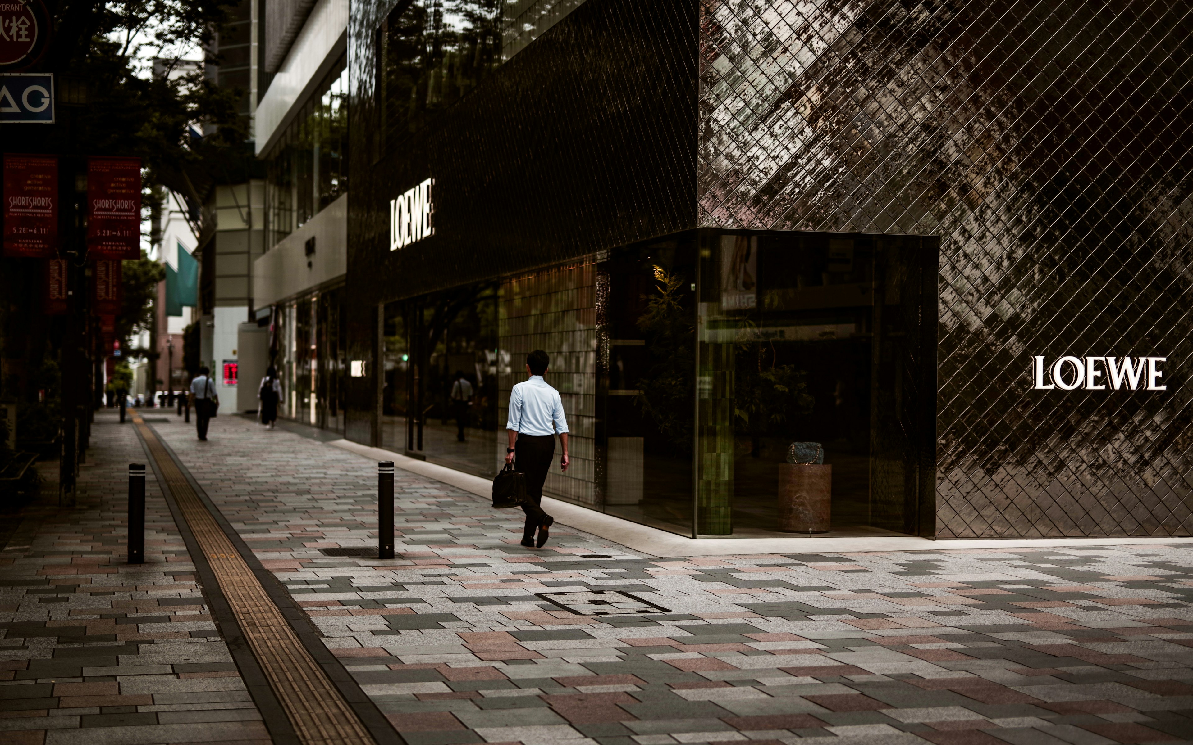 A businessman walking past a Loewe store in a modern urban setting