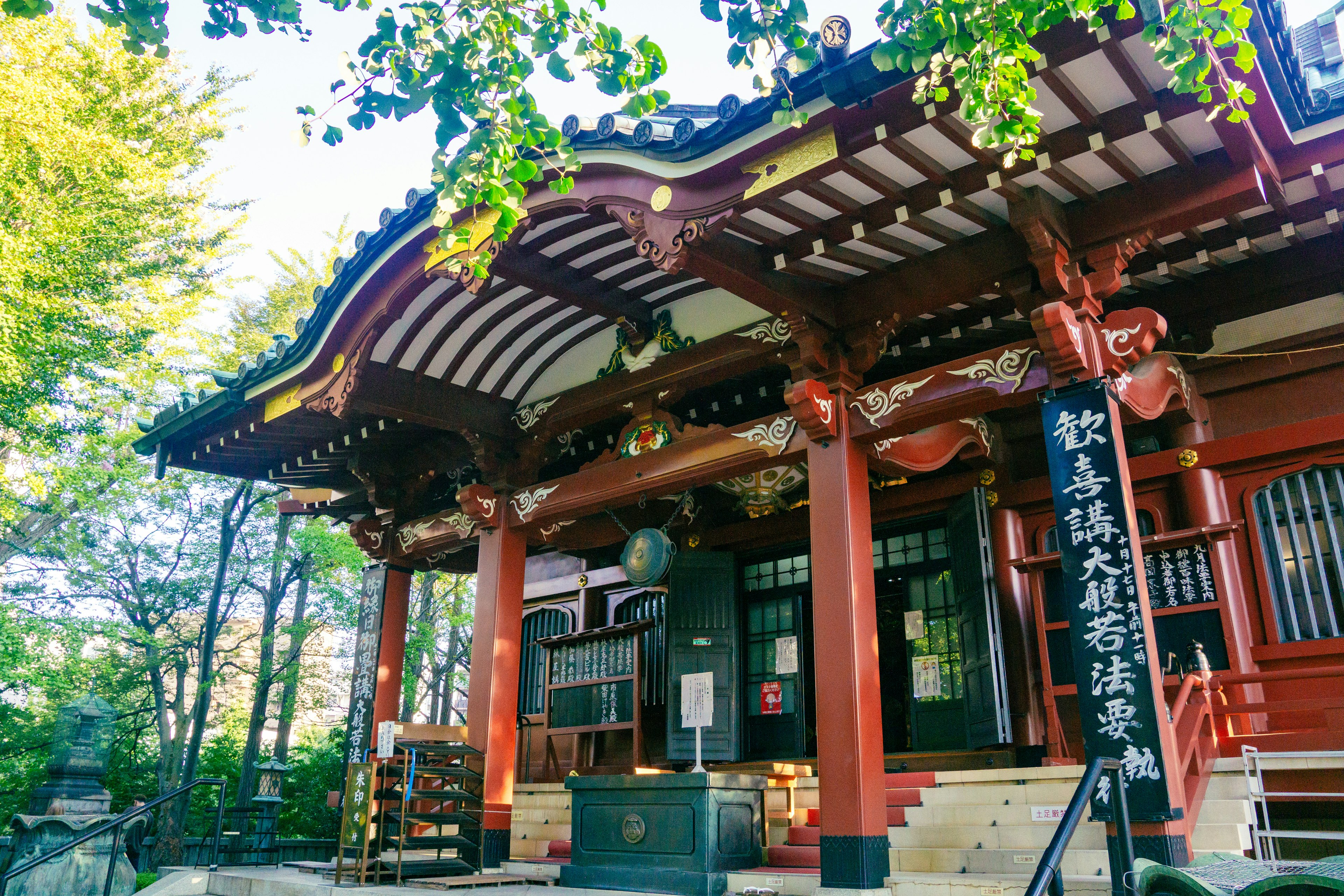 Hermosa fachada de un templo japonés con pilares rojos y techo decorativo rodeado de árboles verdes