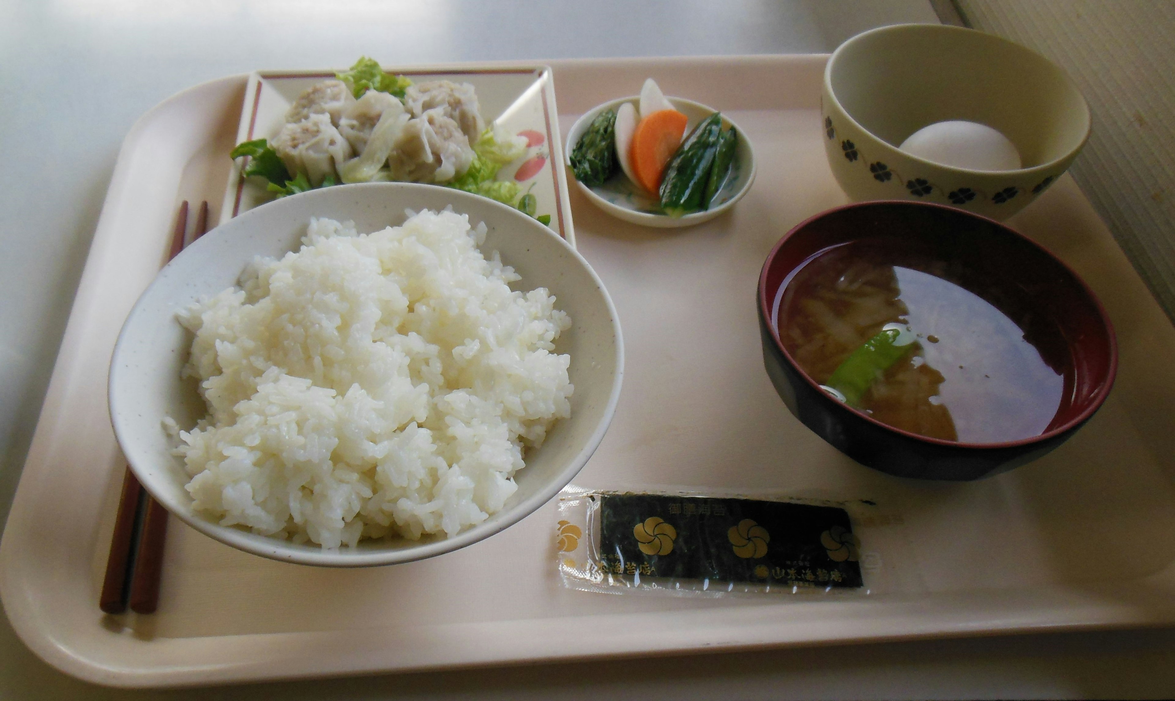 Tray featuring white rice, miso soup, vegetable side dishes, boiled egg, and a sweet dessert