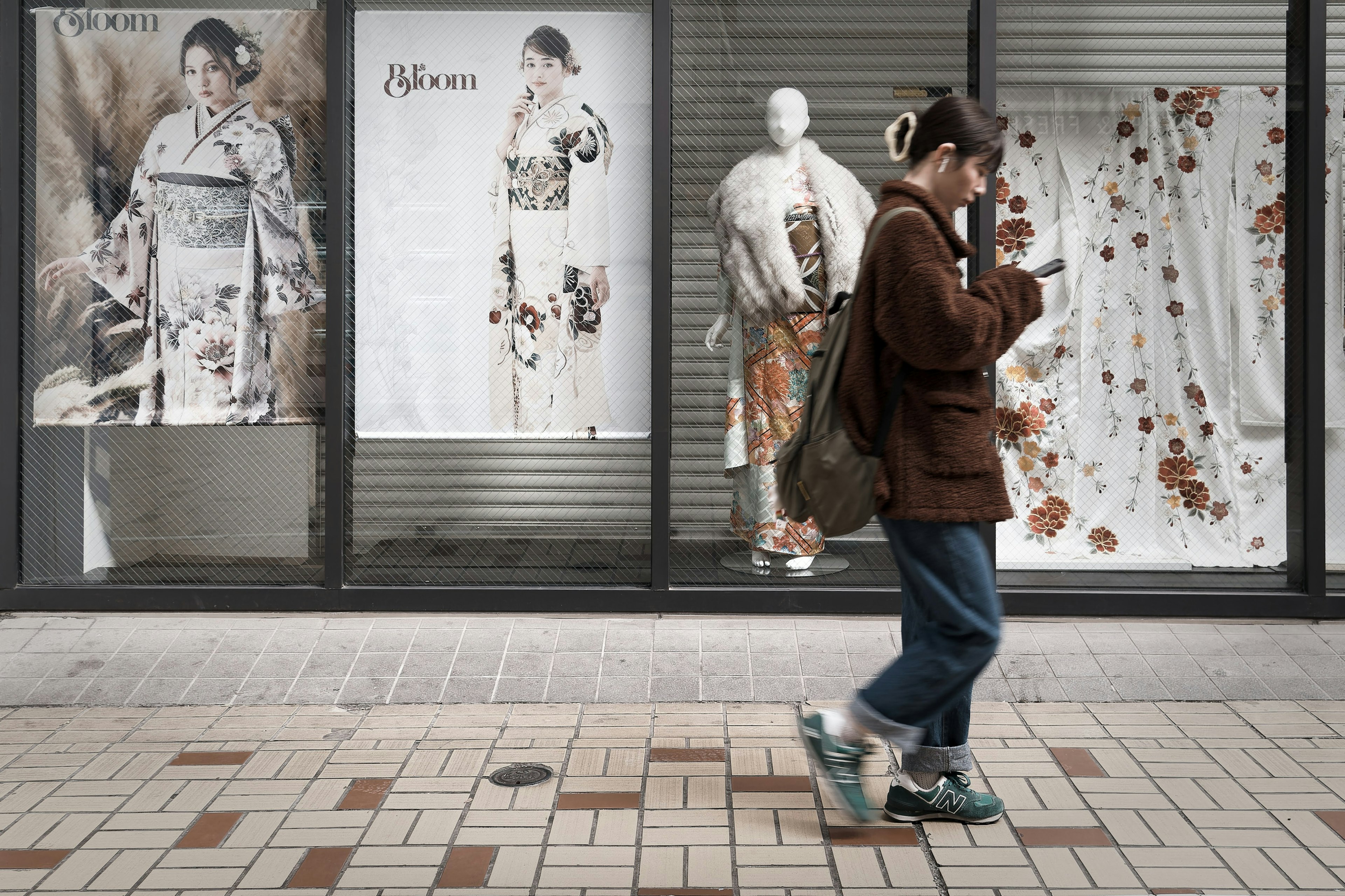 一位年輕女性在街上行走，商店櫥窗中有和服展示