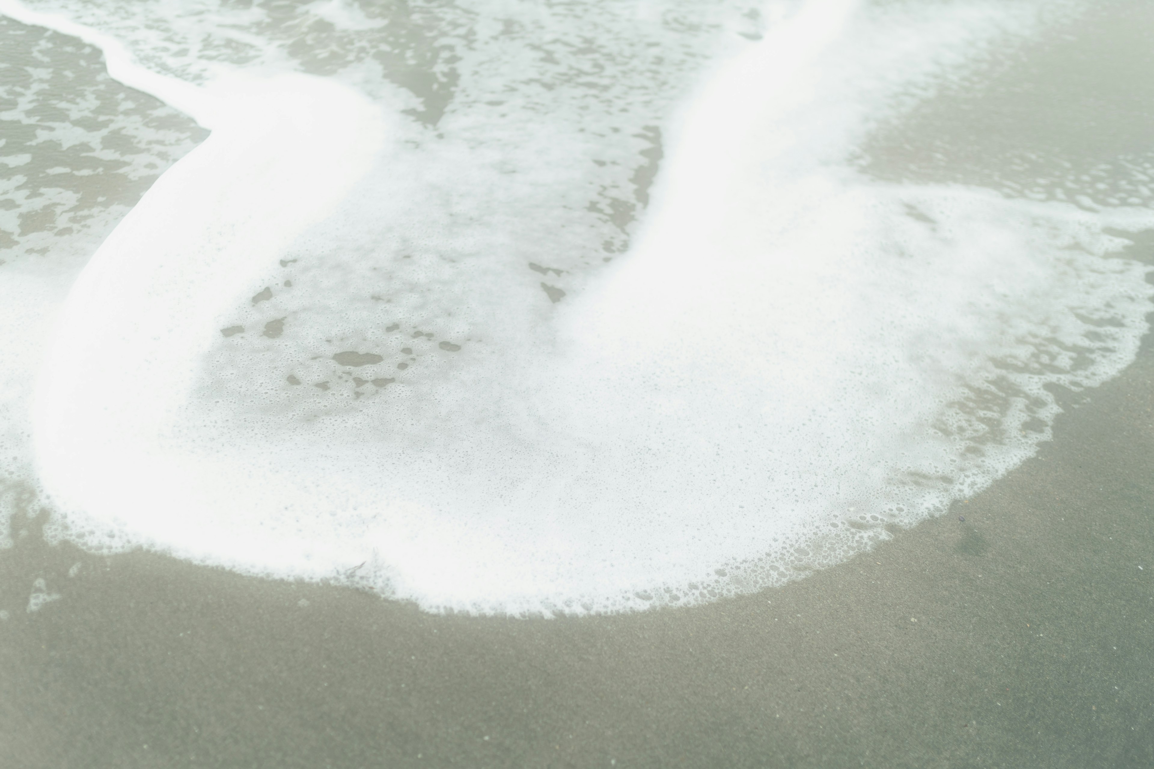 Waves crashing on the shore with white foam and sandy beach