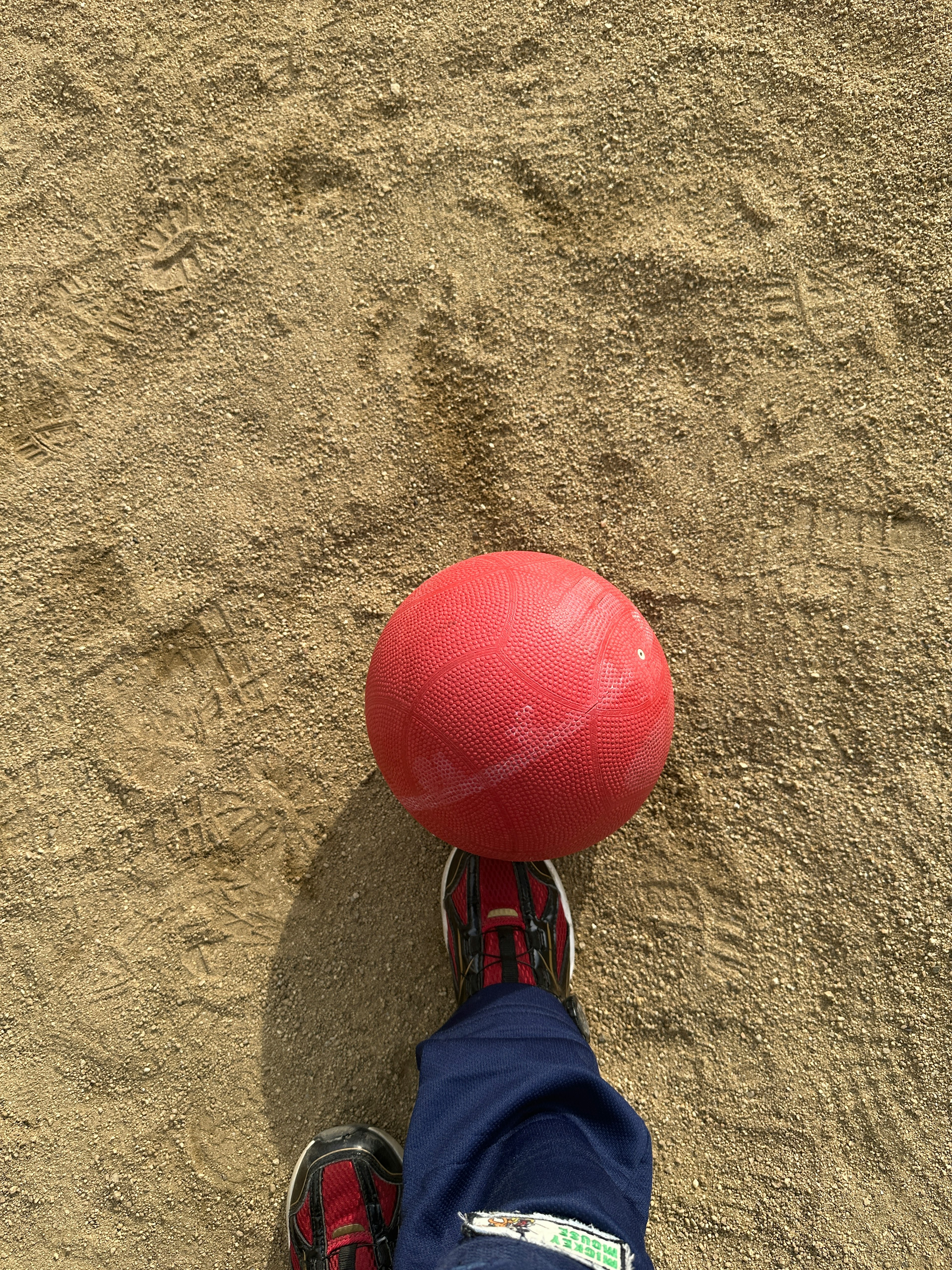 Balle rouge sur un sol sablonneux avec un pied visible