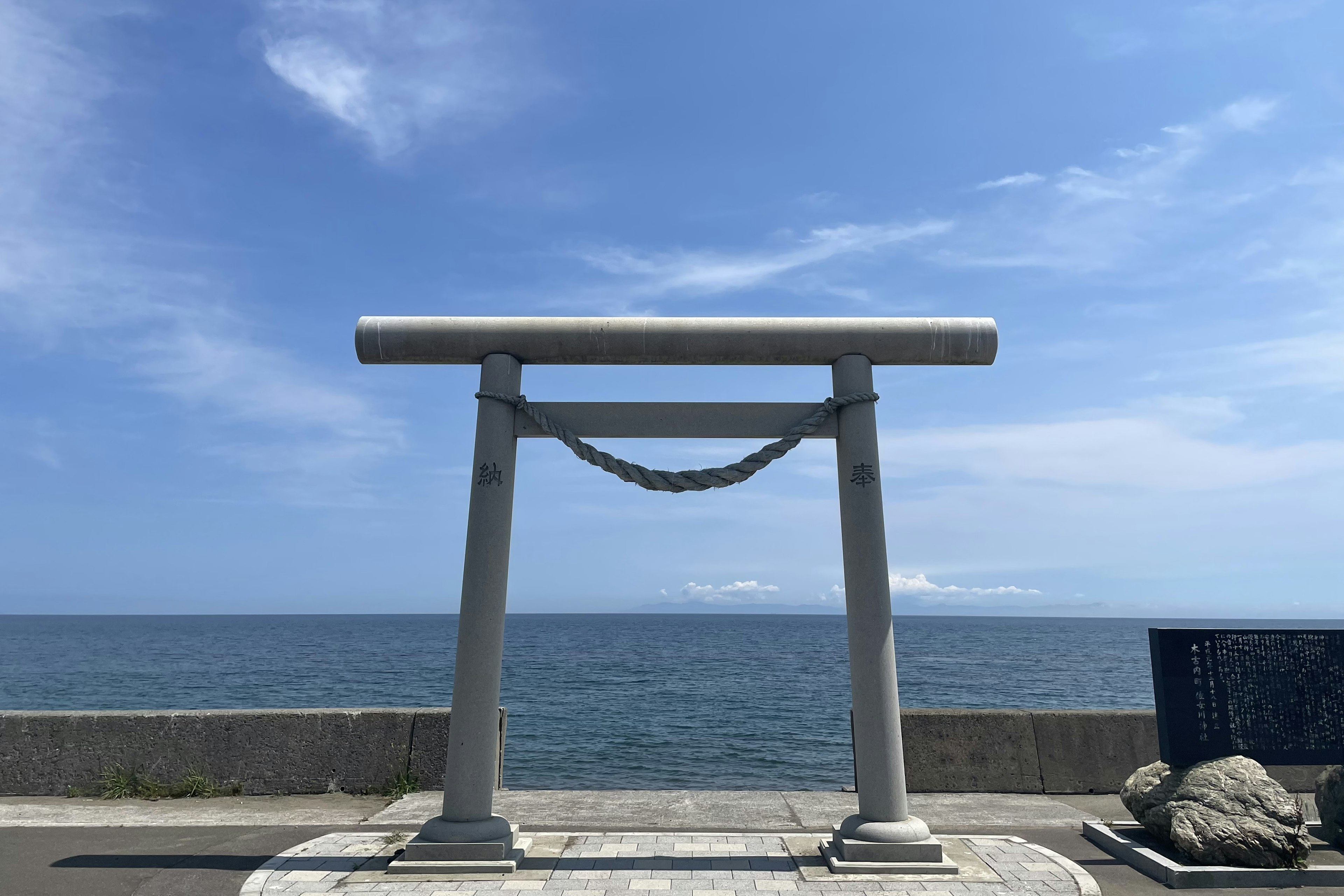 青い空と海の背景に立つ白い鳥居と岩