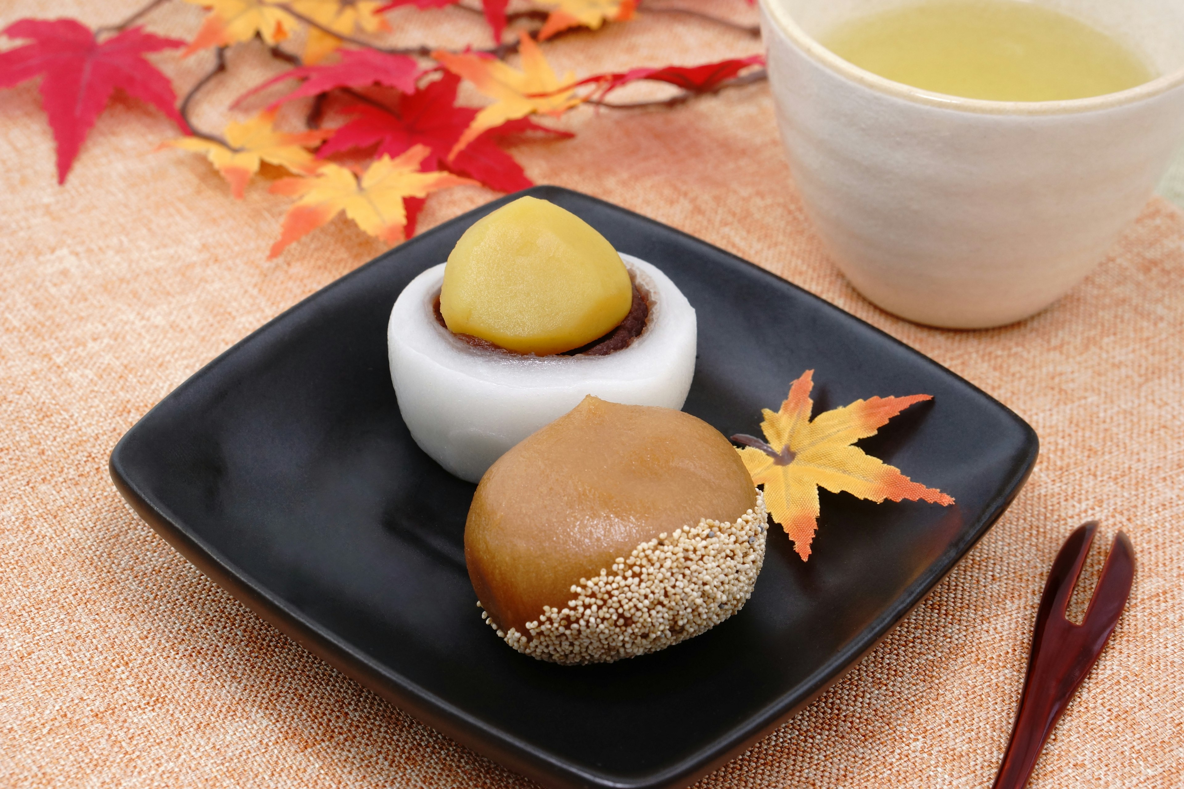 Plate of traditional Japanese sweets decorated with autumn leaves and a cup of green tea