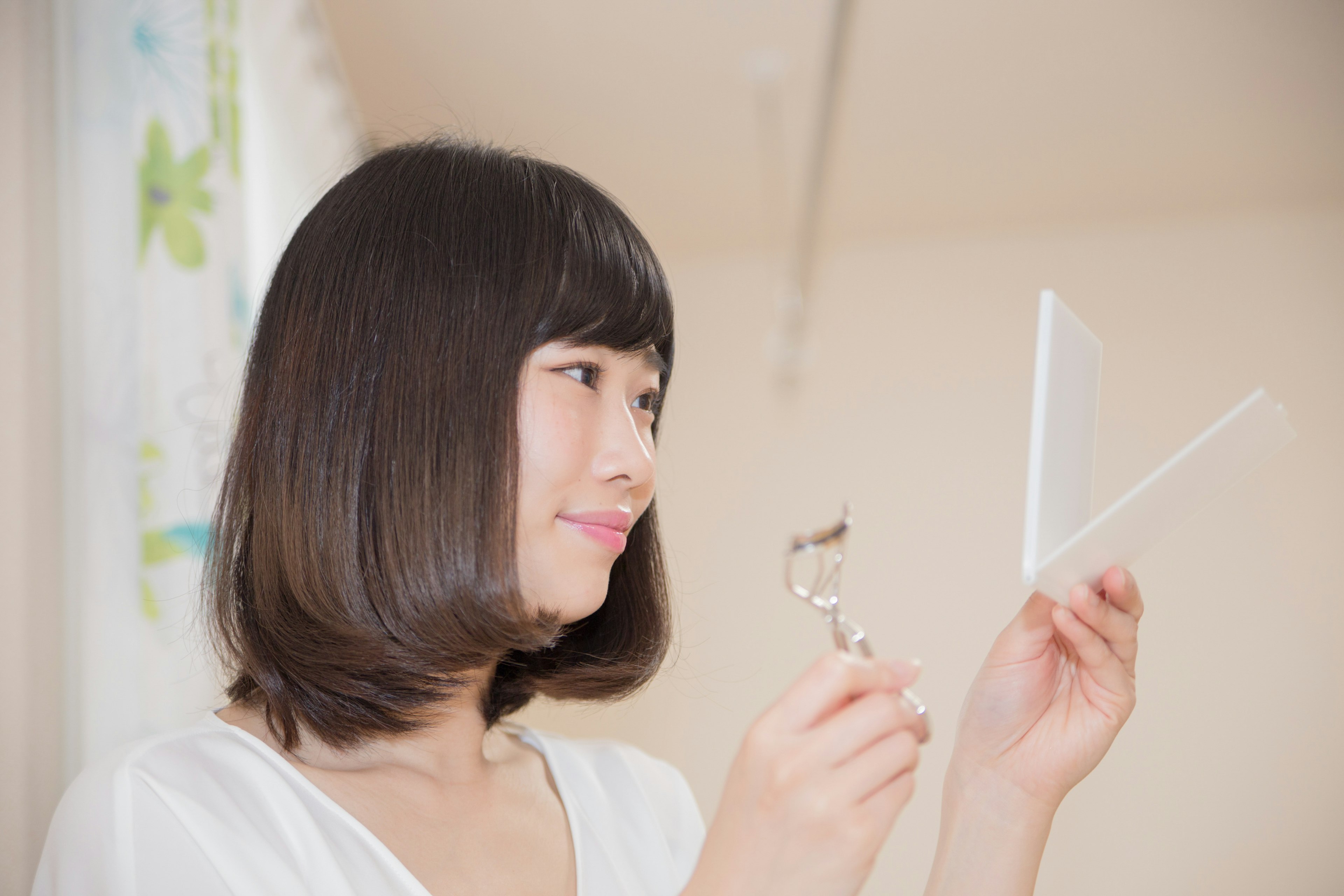 Femme examinant son reflet tout en tenant un recourbe-cils et un miroir