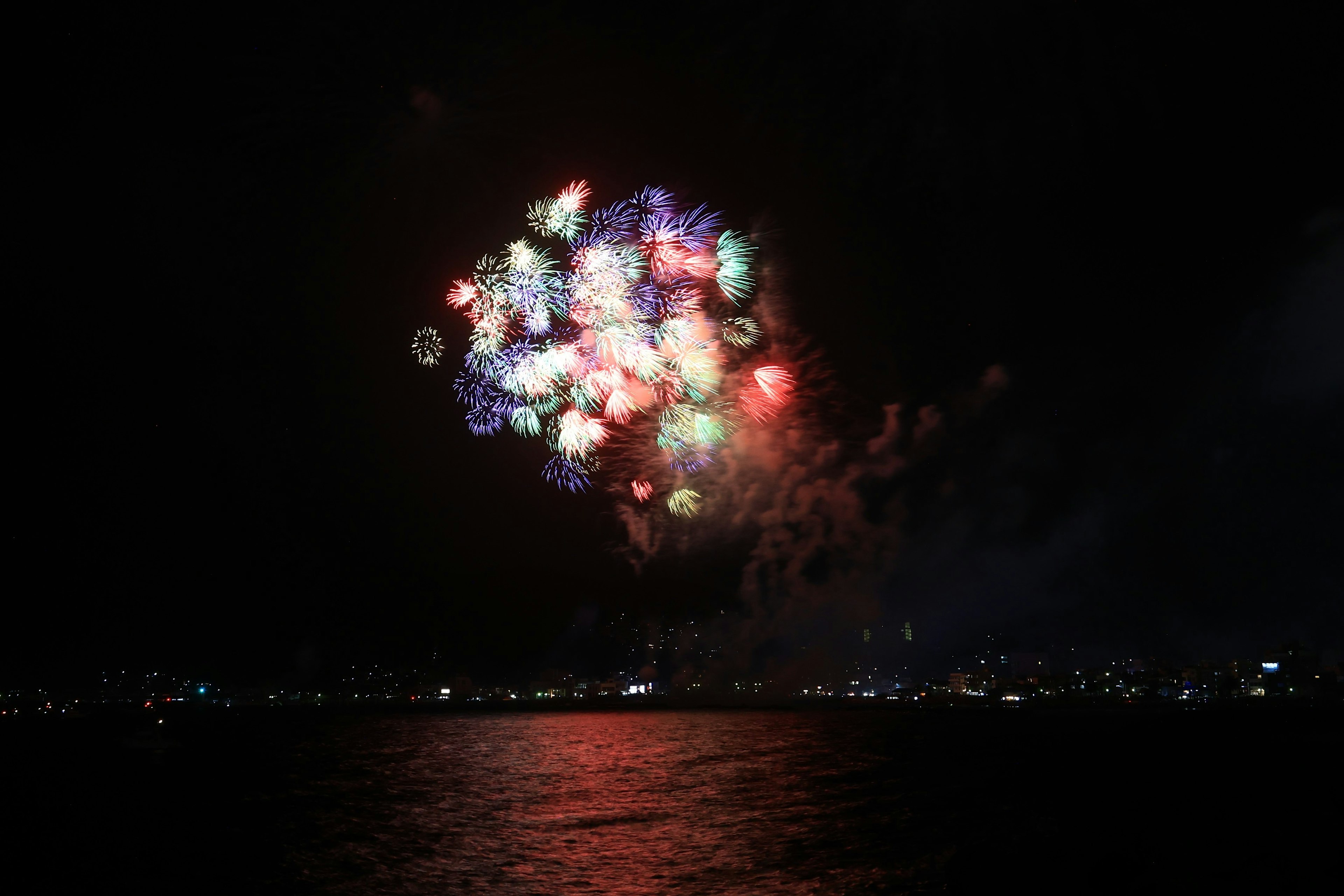 Fuegos artificiales coloridos estallando en el cielo nocturno reflejándose en la superficie del agua