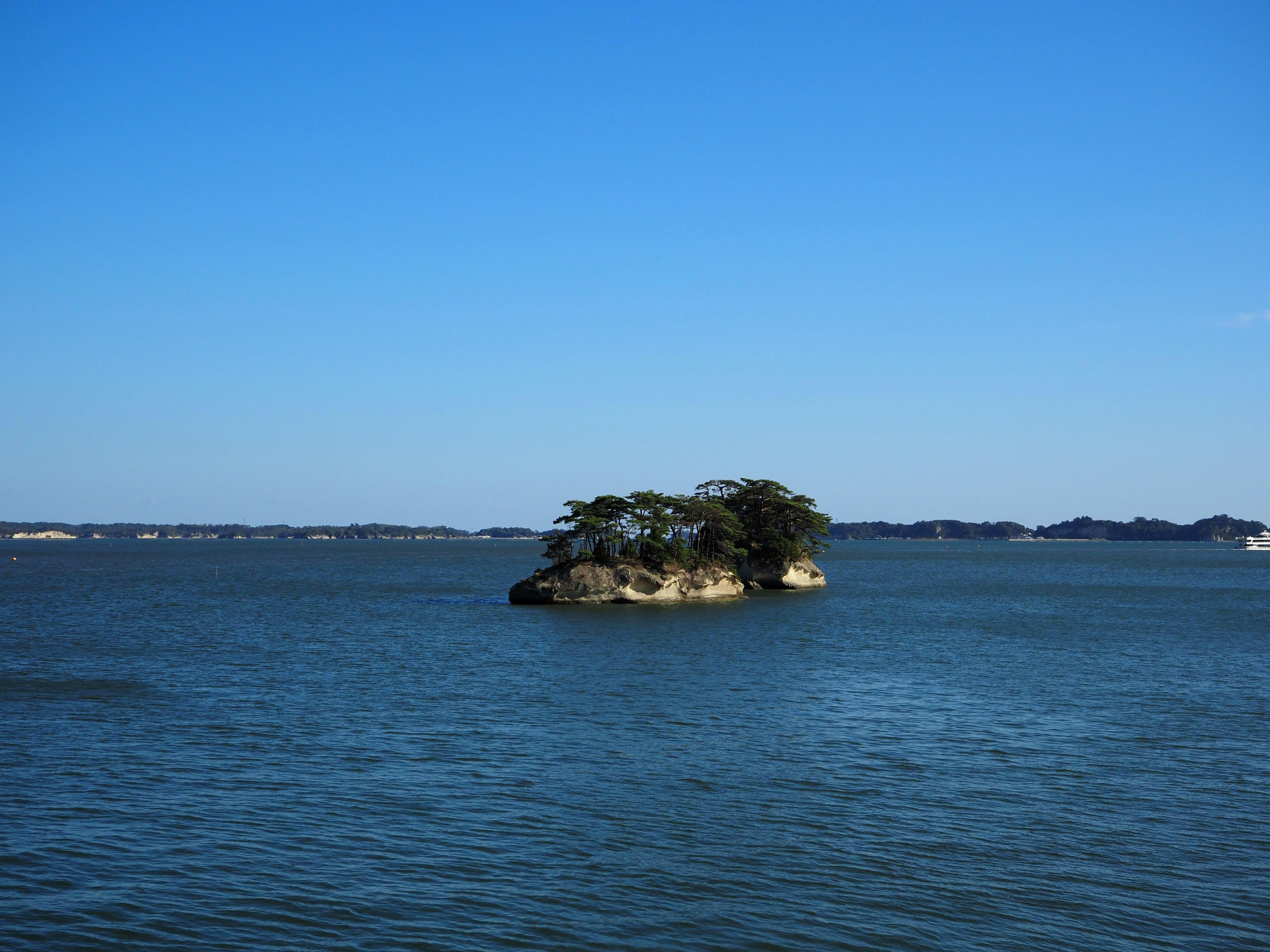 A small island with trees surrounded by calm water under a blue sky