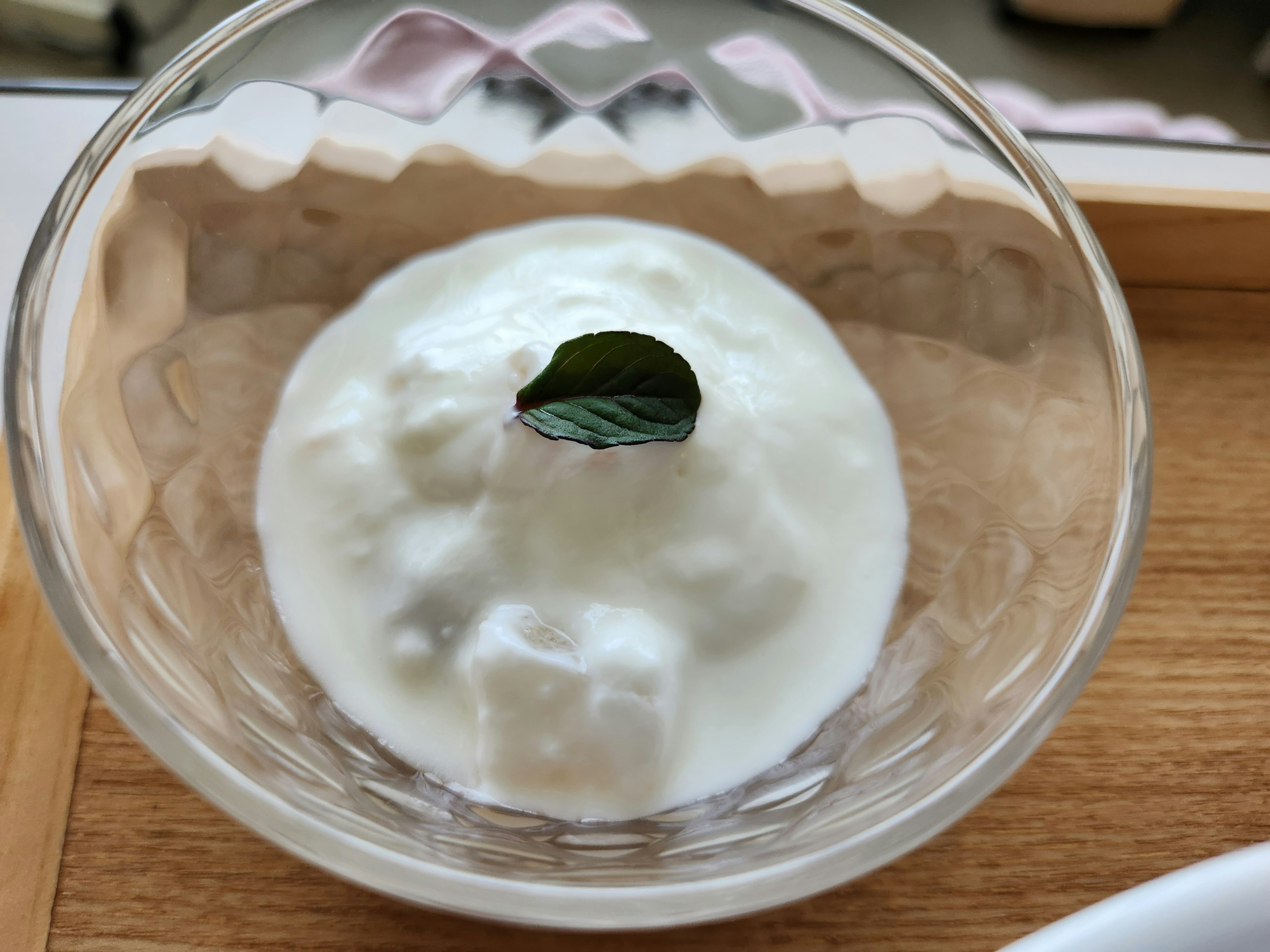 Postre de yogur cremoso decorado con una hoja de menta en un tazón simple