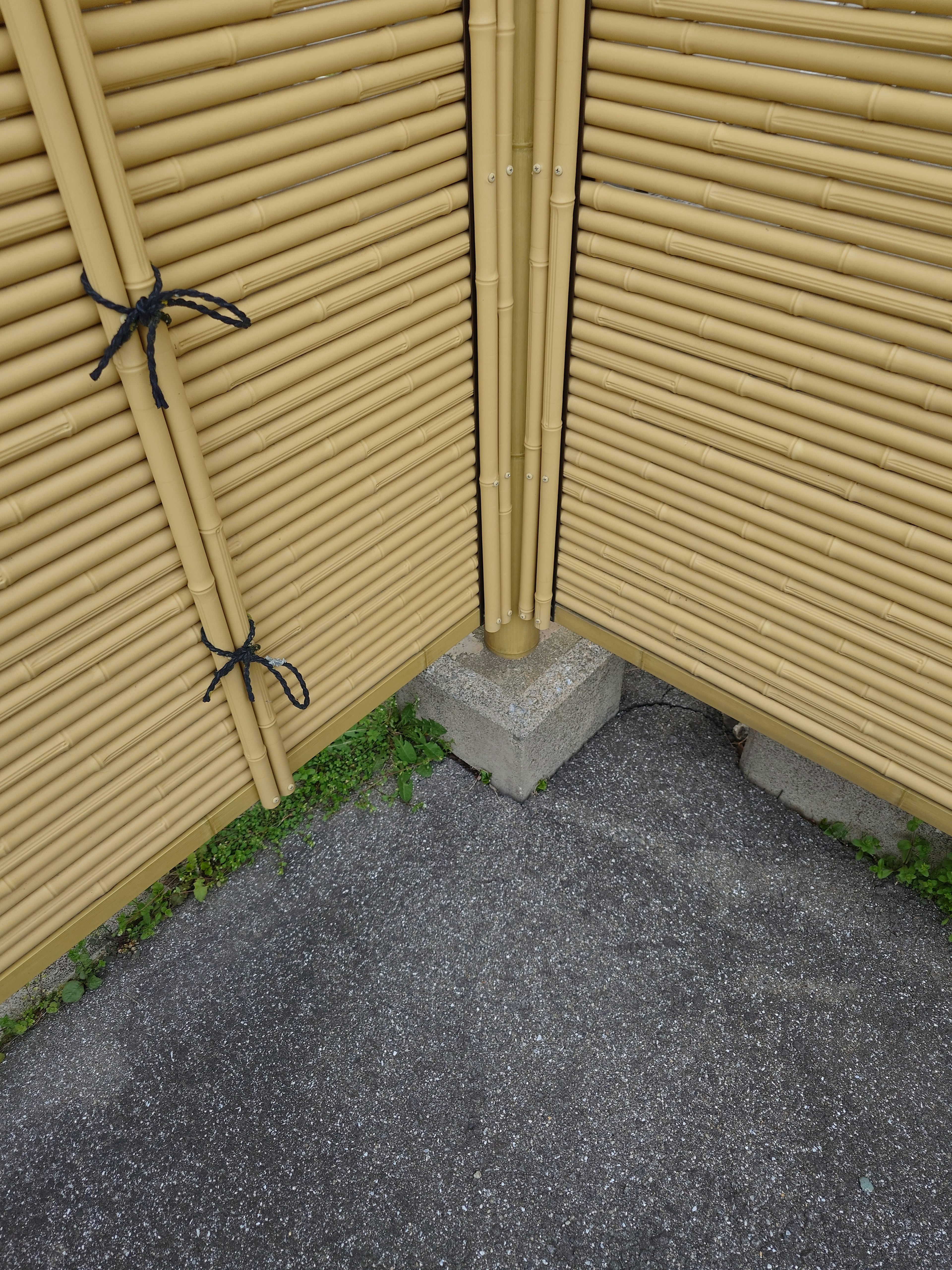 Esquina de una cerca de bambú amarillo asegurada con lazos sobre un bloque de concreto