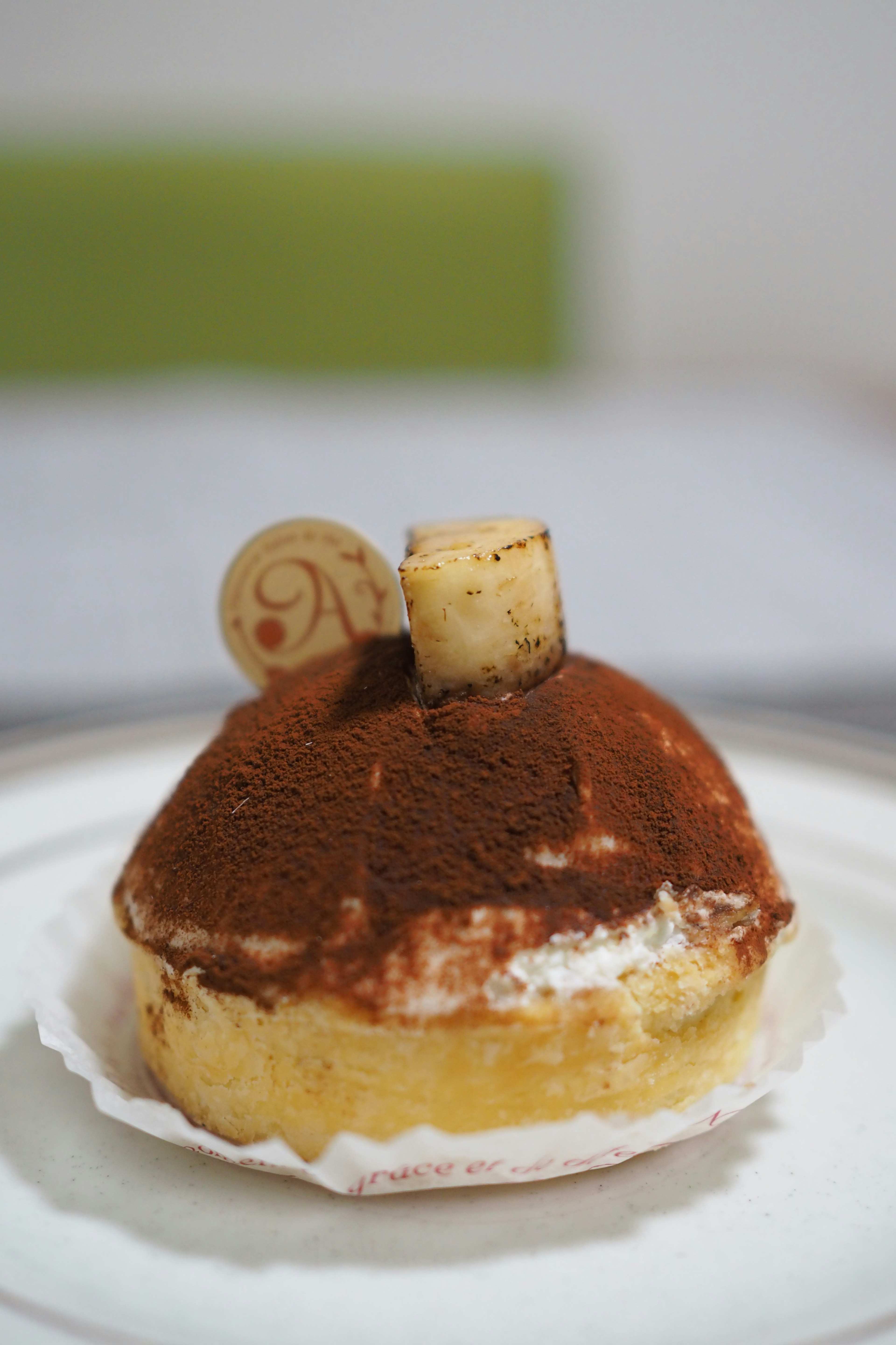 A dessert resembling tiramisu sits on a plate featuring creamy layers and cocoa powder topping