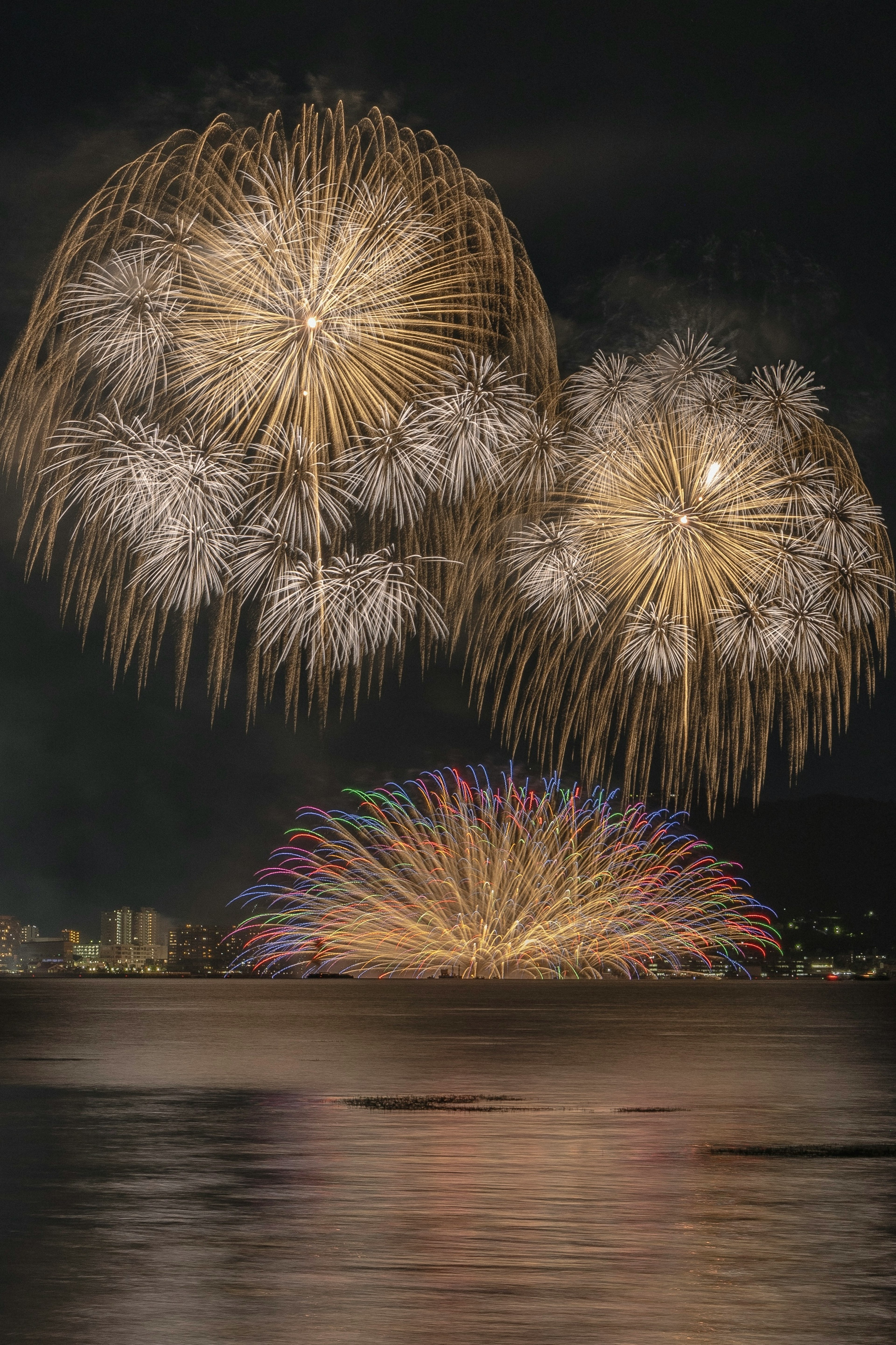 Un'esplosione di fuochi d'artificio nel cielo notturno con riflessi sull'acqua