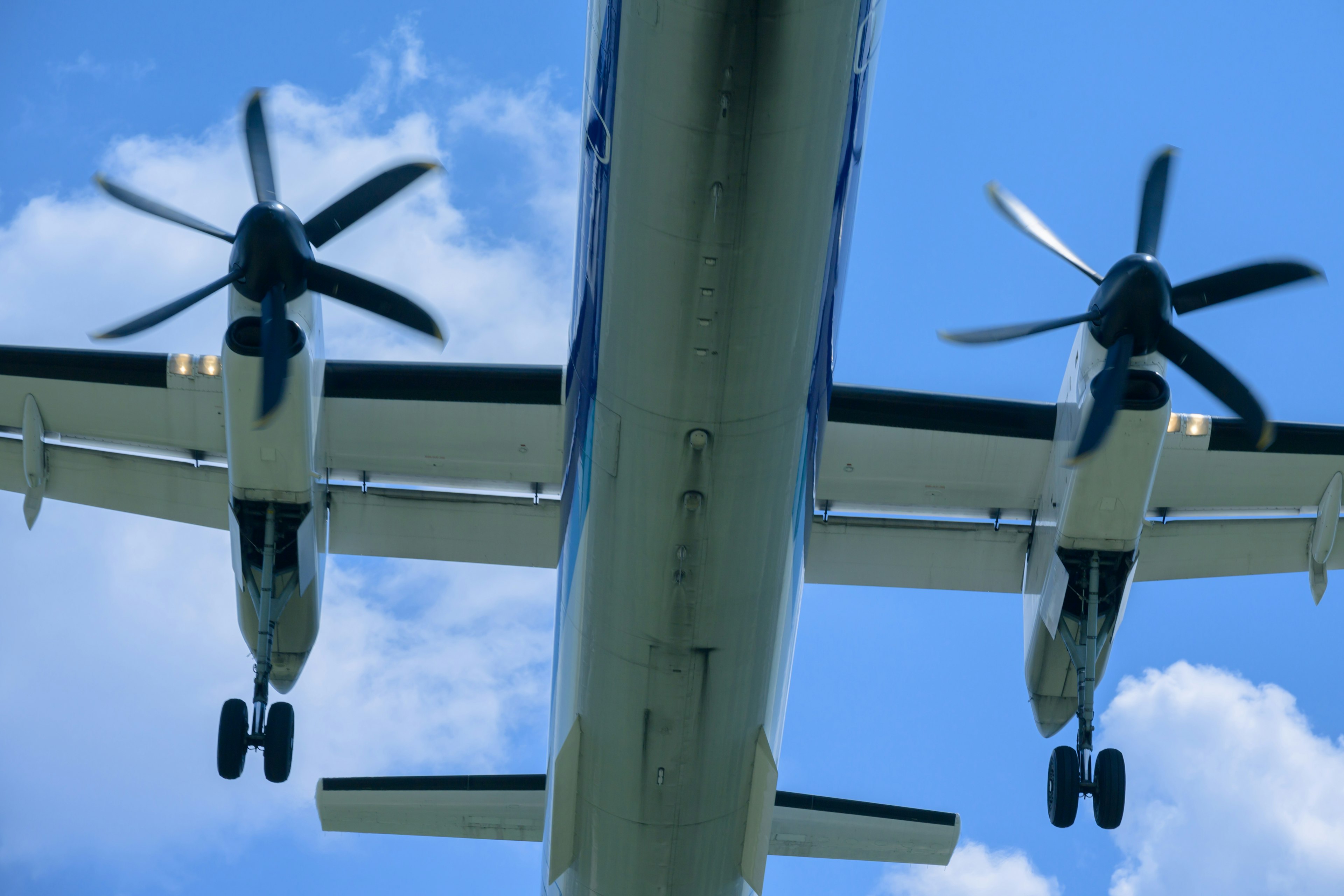 Vista inferior de un avión de hélice con cielo azul y nubes blancas