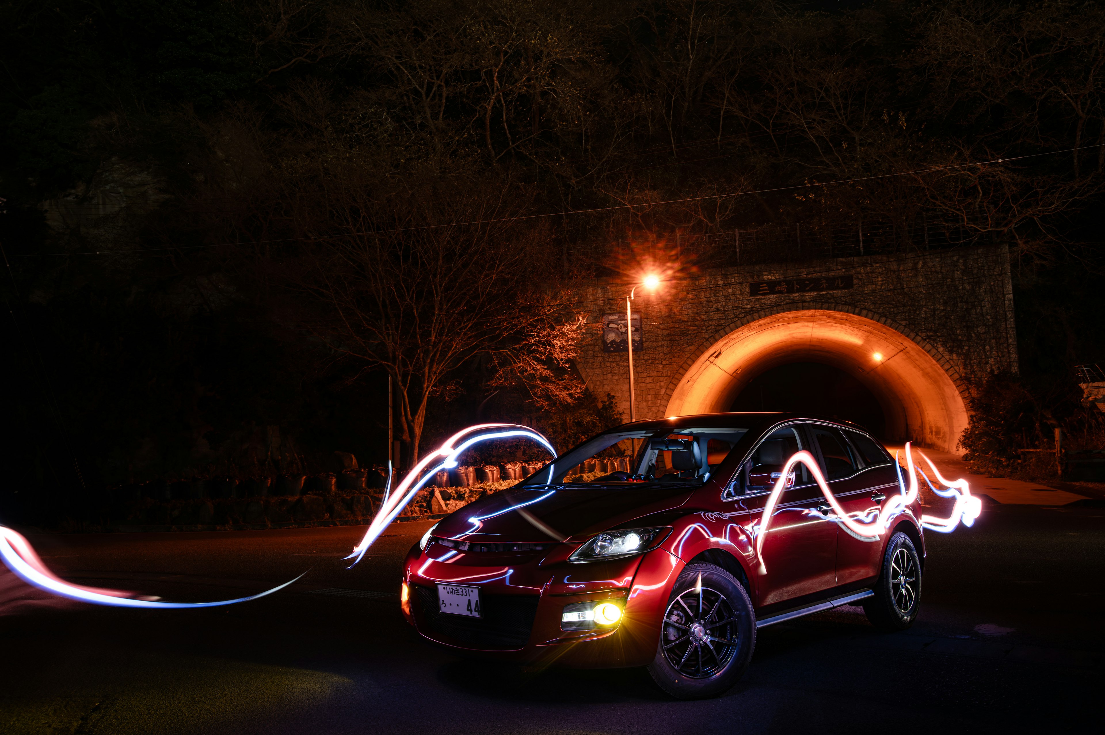 夜のトンネルの前に停まった赤い車と光の軌跡