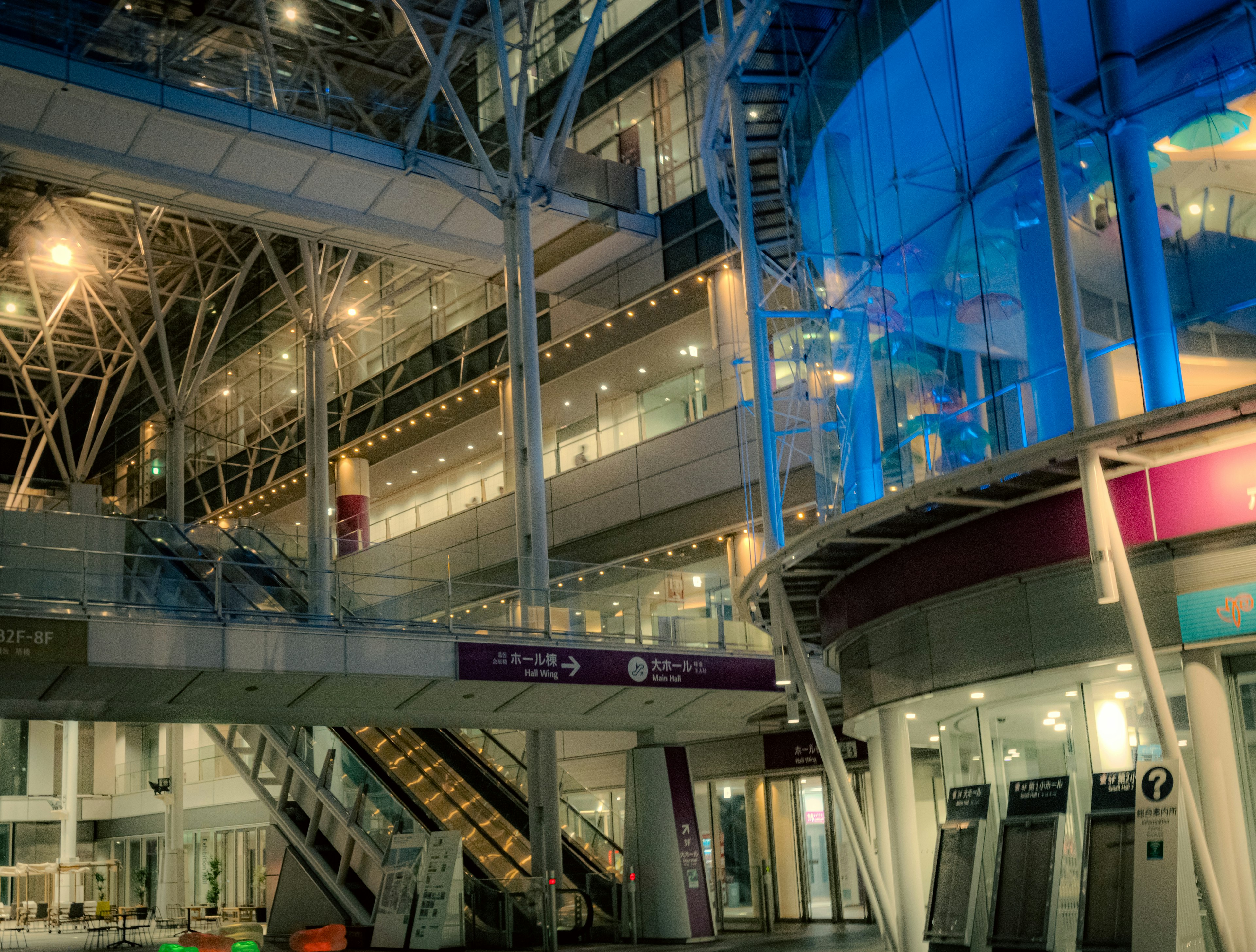 Modern interior of a building with blue lighting and glass walls featuring stairs and elevators