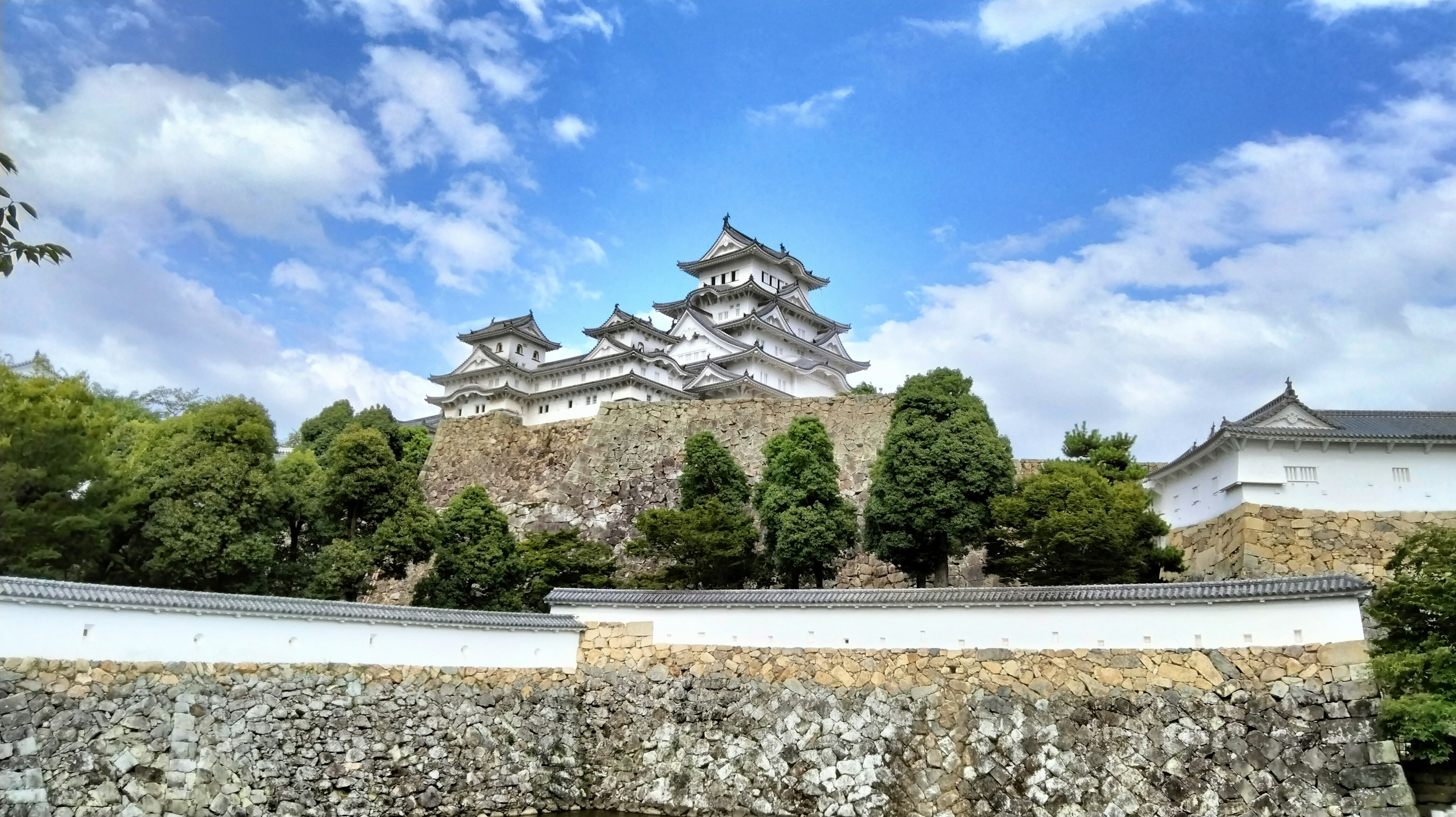 Kastil Himeji dikelilingi oleh pepohonan dan langit biru