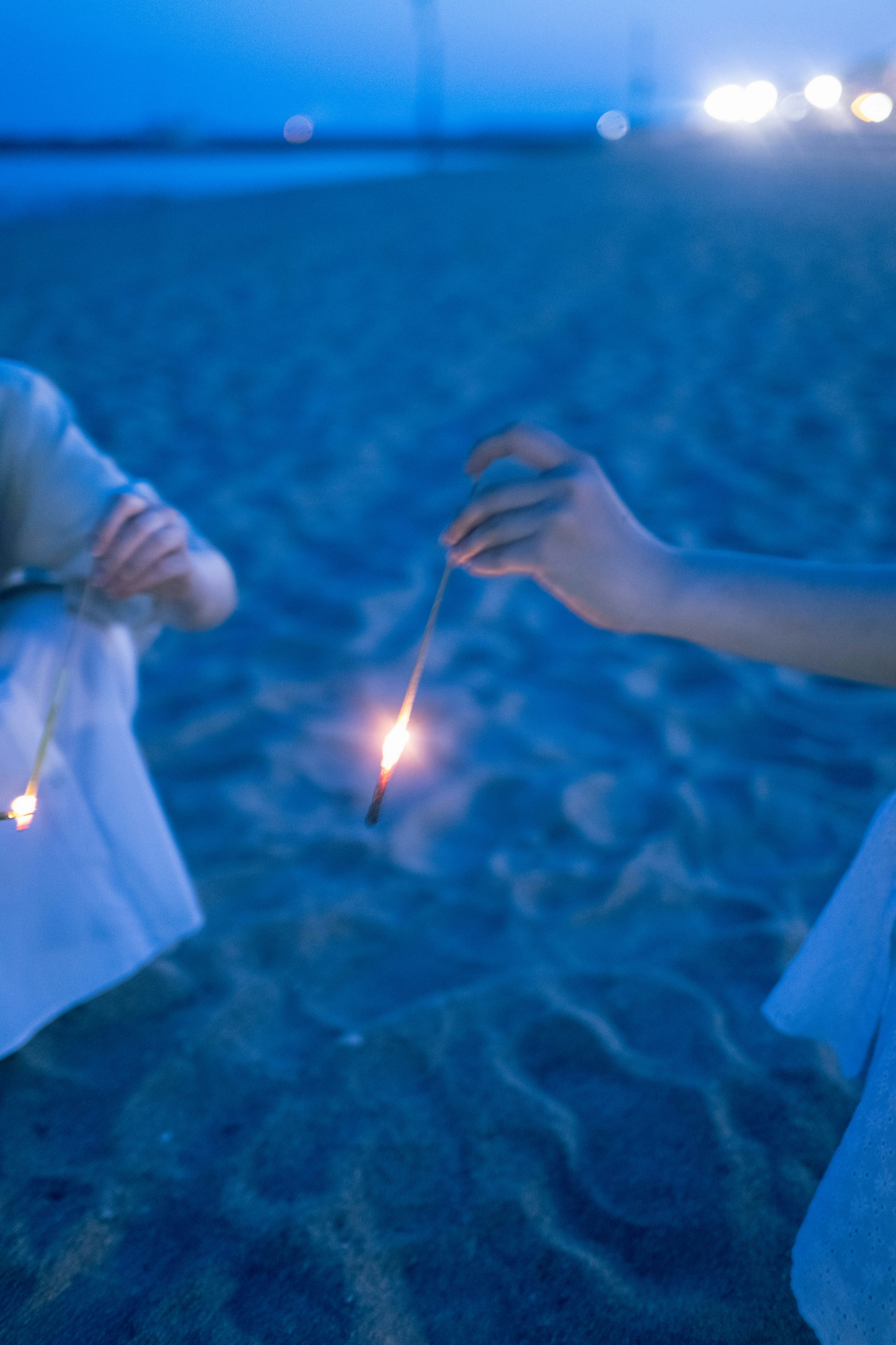 Hand hält ein Feuerwerk an einem Strand bei Nacht