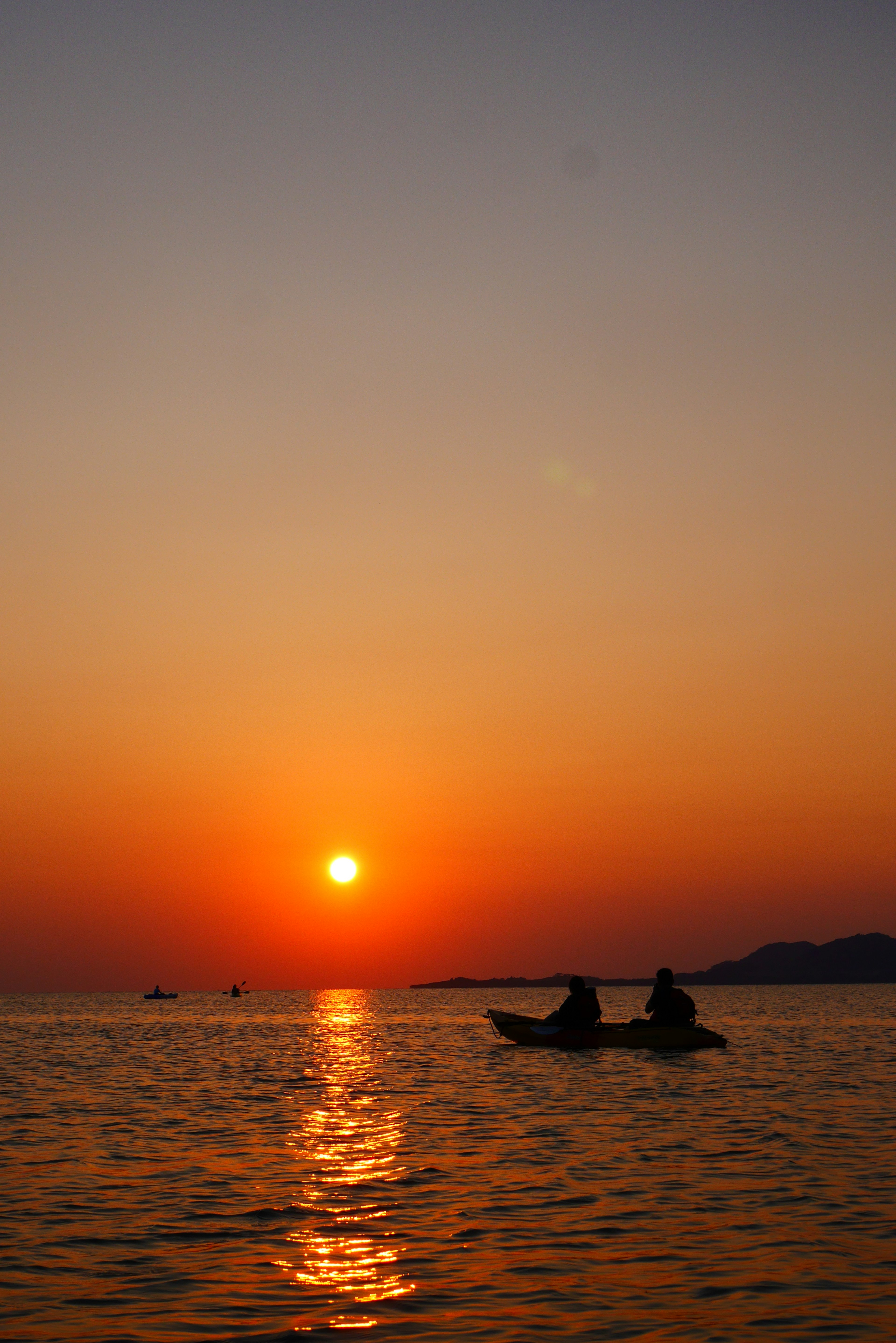 Silhouette von zwei Personen, die im Meer mit Sonnenuntergang im Hintergrund Kajak fahren