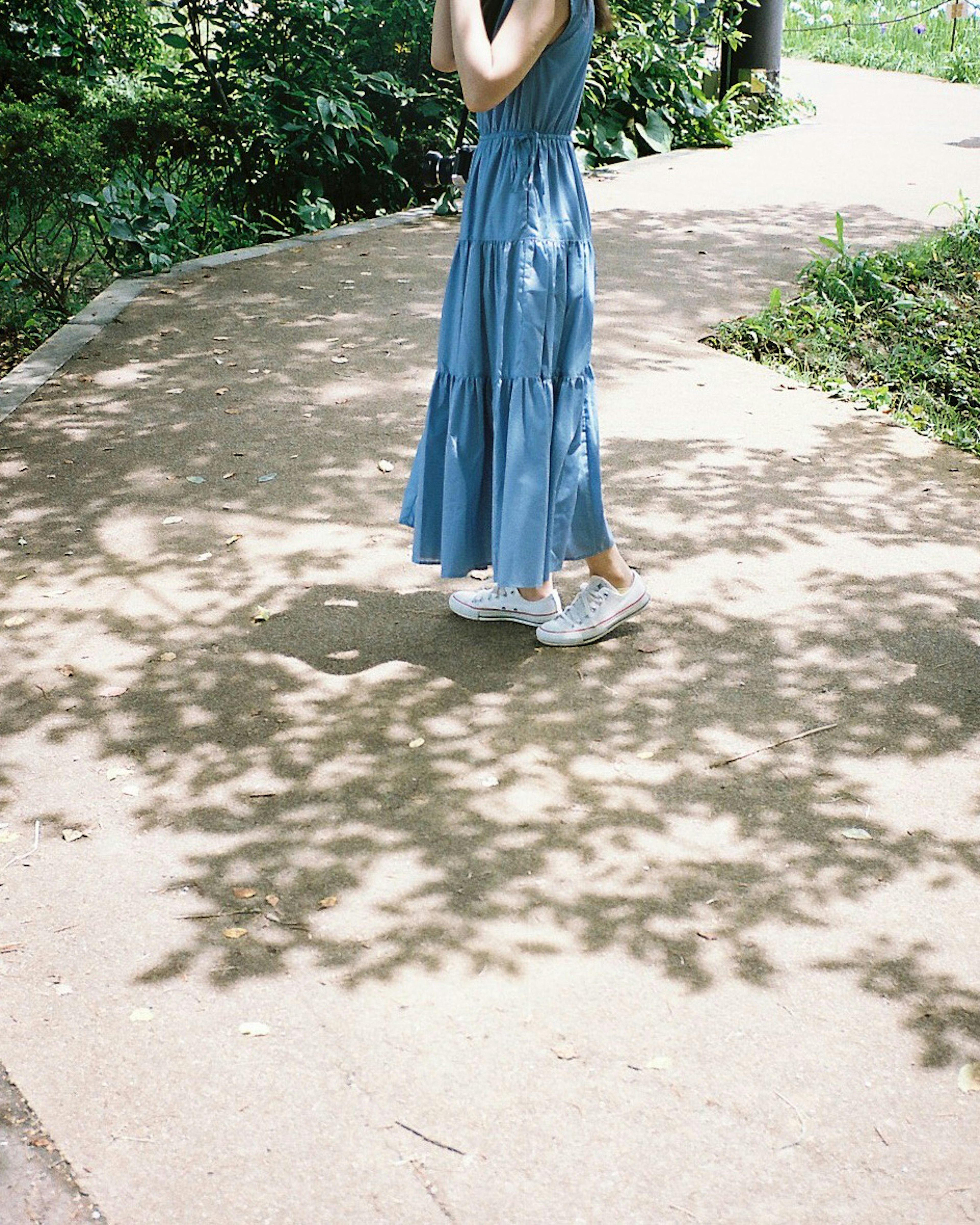 Woman in a blue dress walking on a path with shadows