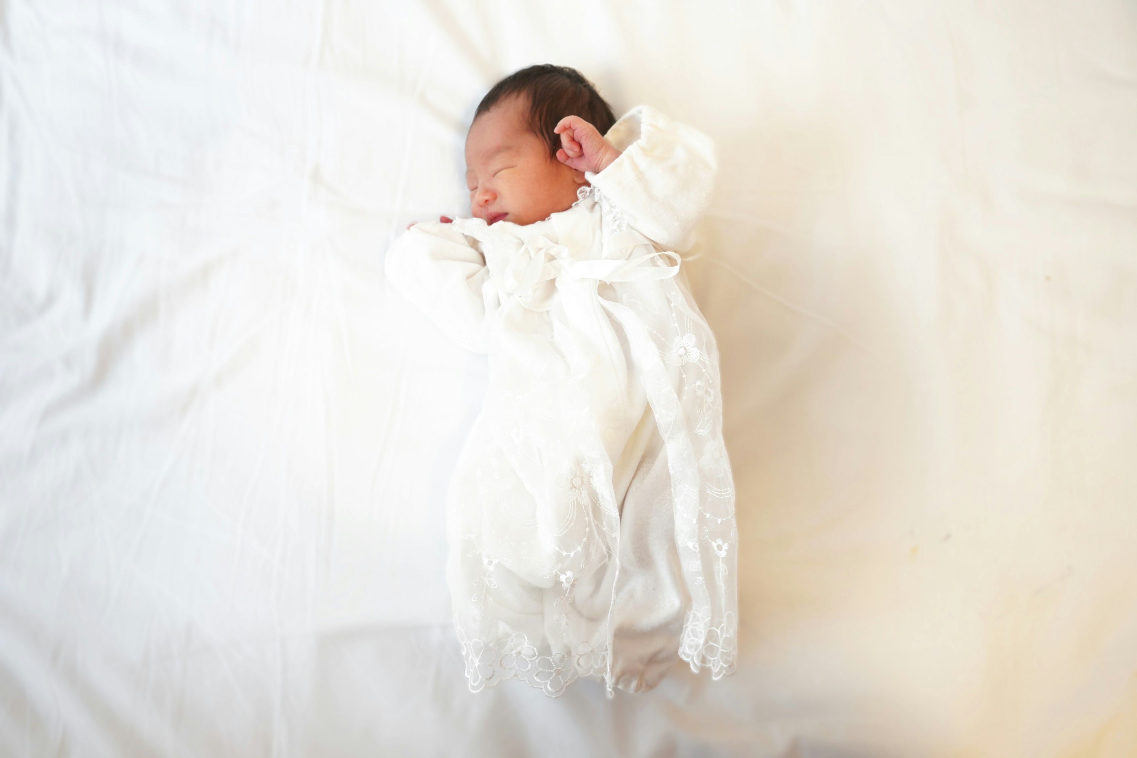 Bayi yang tidur di atas selimut putih mengenakan pakaian putih yang lucu