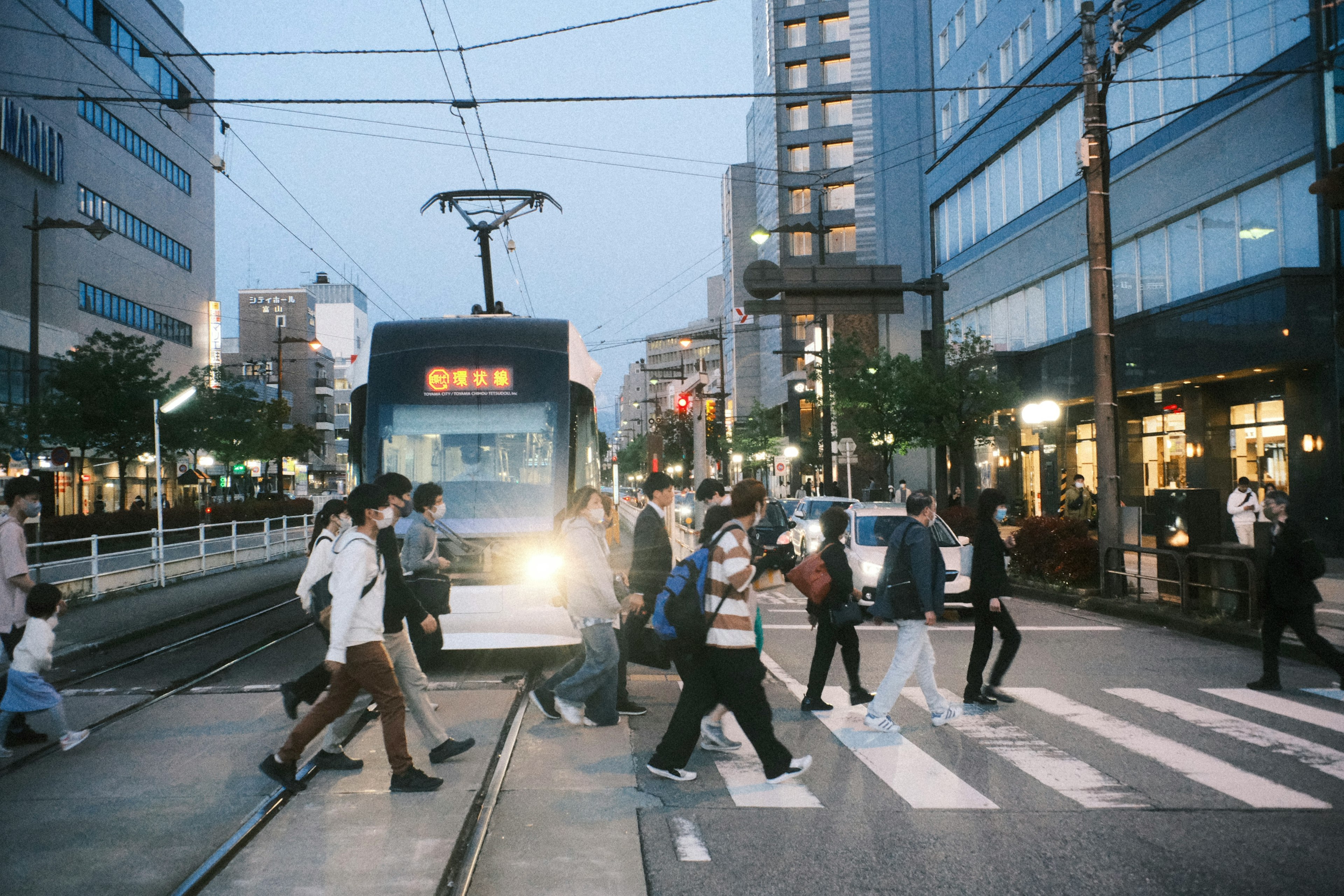 夜の都市で人々が横断歩道を渡る ショッピング街とトラムが見える